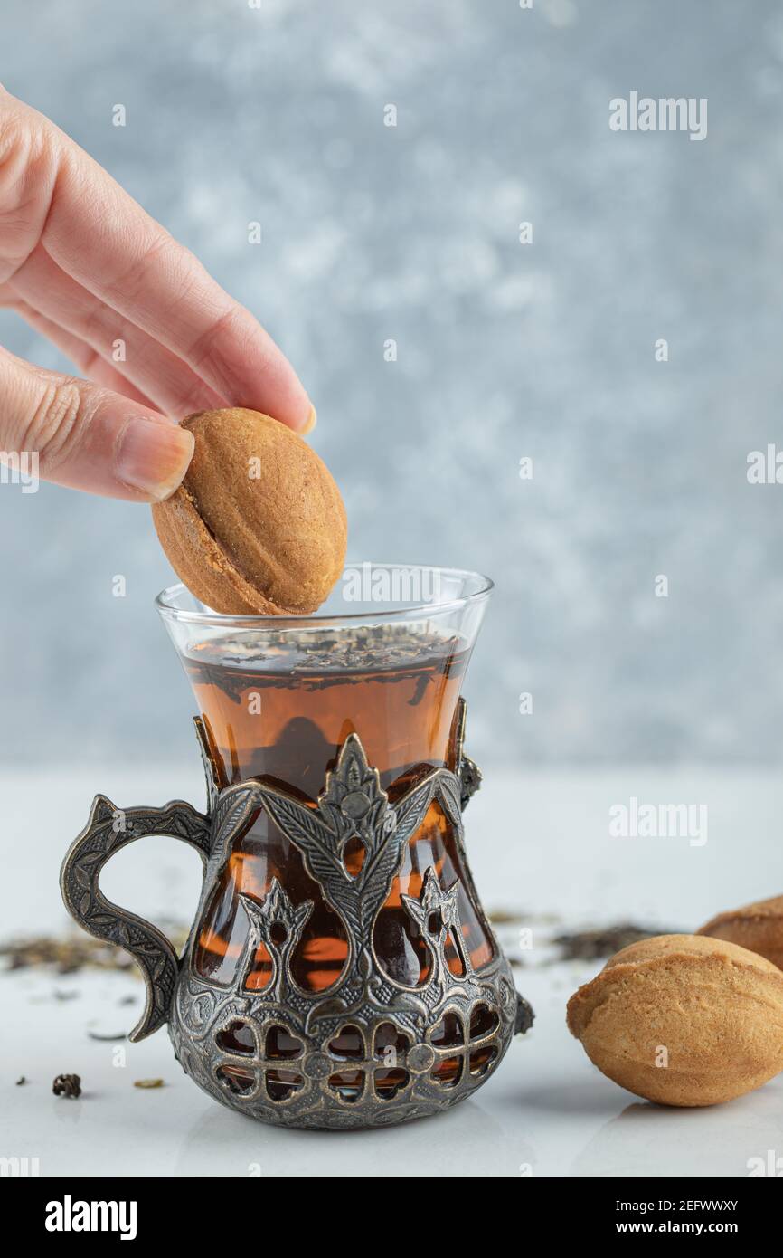 Mano femminile che immergi un biscotto a forma di noce dolce in tazza di tè Foto Stock