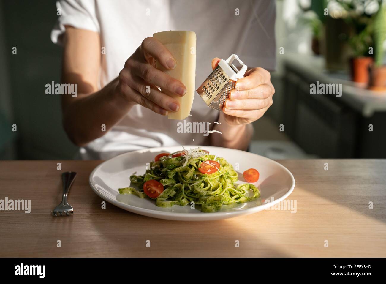 Primo piano di mani di donna che grattugiano il parmigiano in pasta con pesto di salsa, pomodori ciliegini freschi. Foto Stock