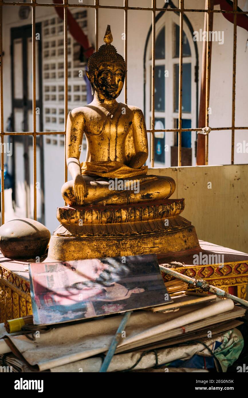 Statua dorata del buddha danneggiata seduta dietro un mucchio di carte e libri con luce dorata che risplende dentro. Foto Stock