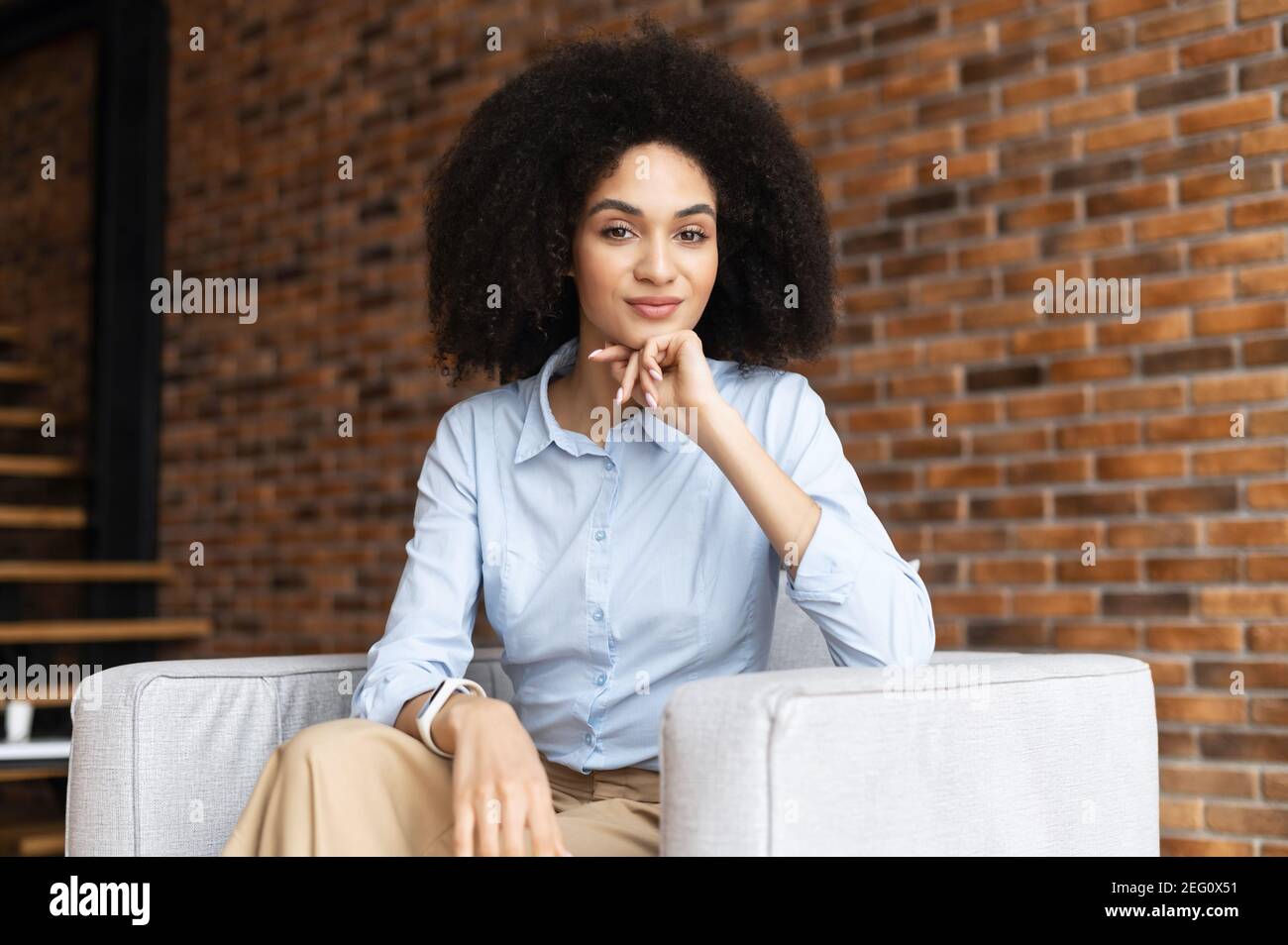 Giovane imprenditore etnico afro-americano di successo con acconciatura Afro in abiti casual, seduto sulla sedia contro Foto Stock