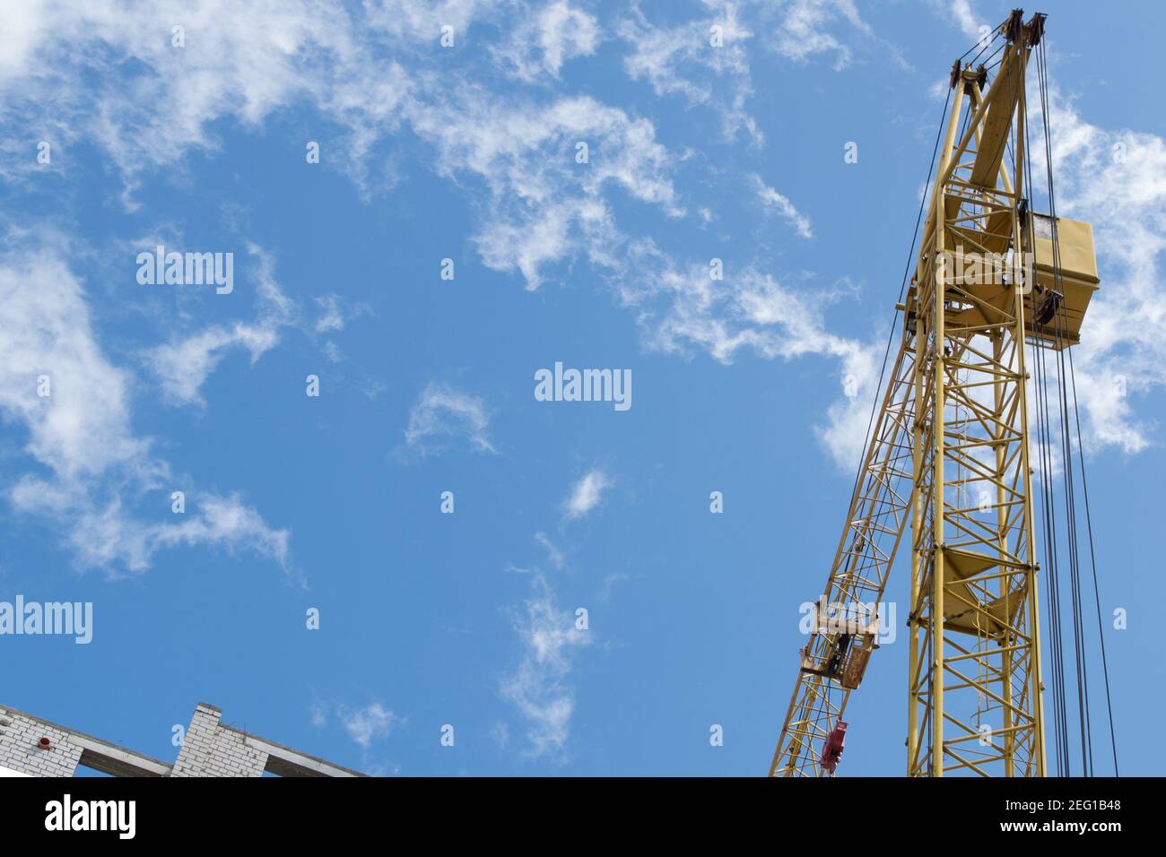 Una gru a torre gialla lavora in un cantiere su i piani superiori di un edificio in mattoni bianchi contro un cielo blu con nuvole fumose e sguazzate Foto Stock