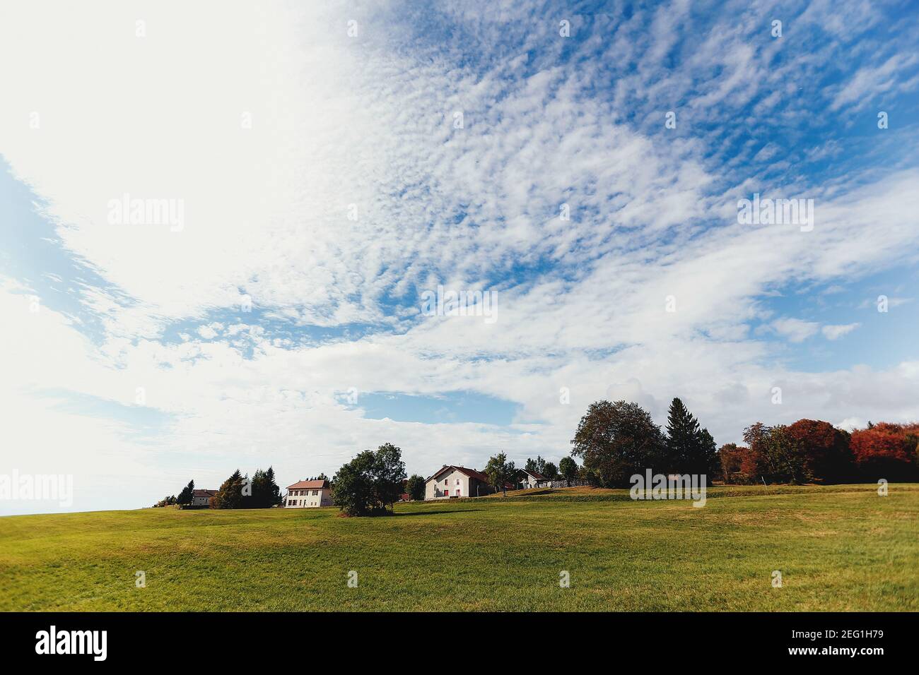 Paesaggio di campi verdi, case private in lontananza, belle nuvole nel cielo Foto Stock