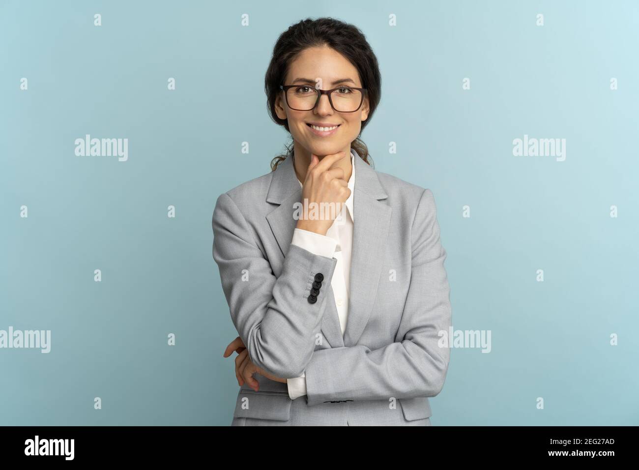 Donna d'affari sicura che tocca il mento e sorride, guardando la telecamera isolata su sfondo blu Foto Stock