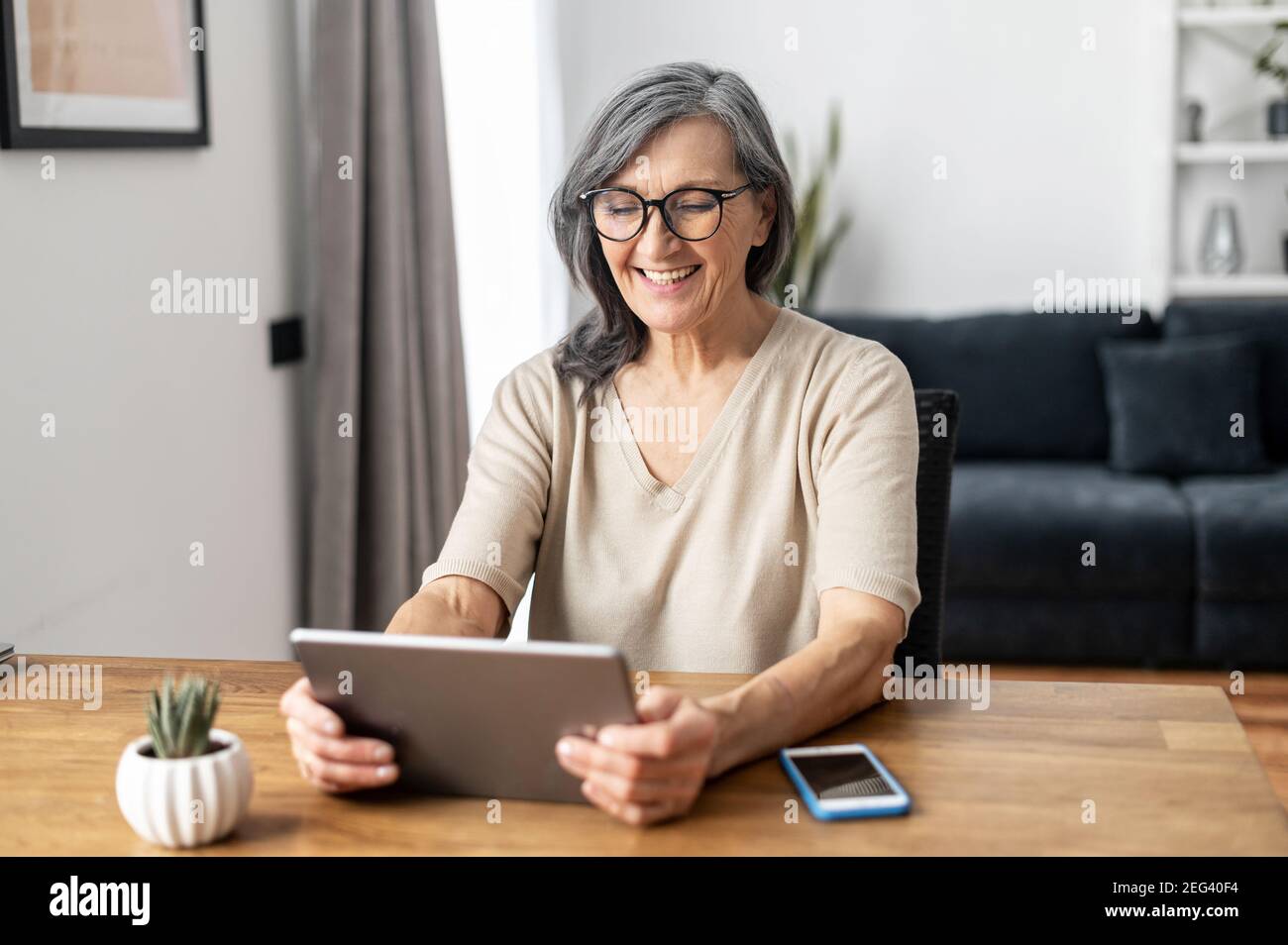 La donna matura e matura di mezza età trascorre il tempo libero a casa utilizzando un tablet digitale. Allegra donna anziana moderna tiene il computer, guardando film divertenti Foto Stock La donna matura e matura di mezza età trascorre il tempo libero a casa utilizzando un tablet digitale. Allegra donna anziana moderna tiene il computer, guardando film divertenti Foto Stock