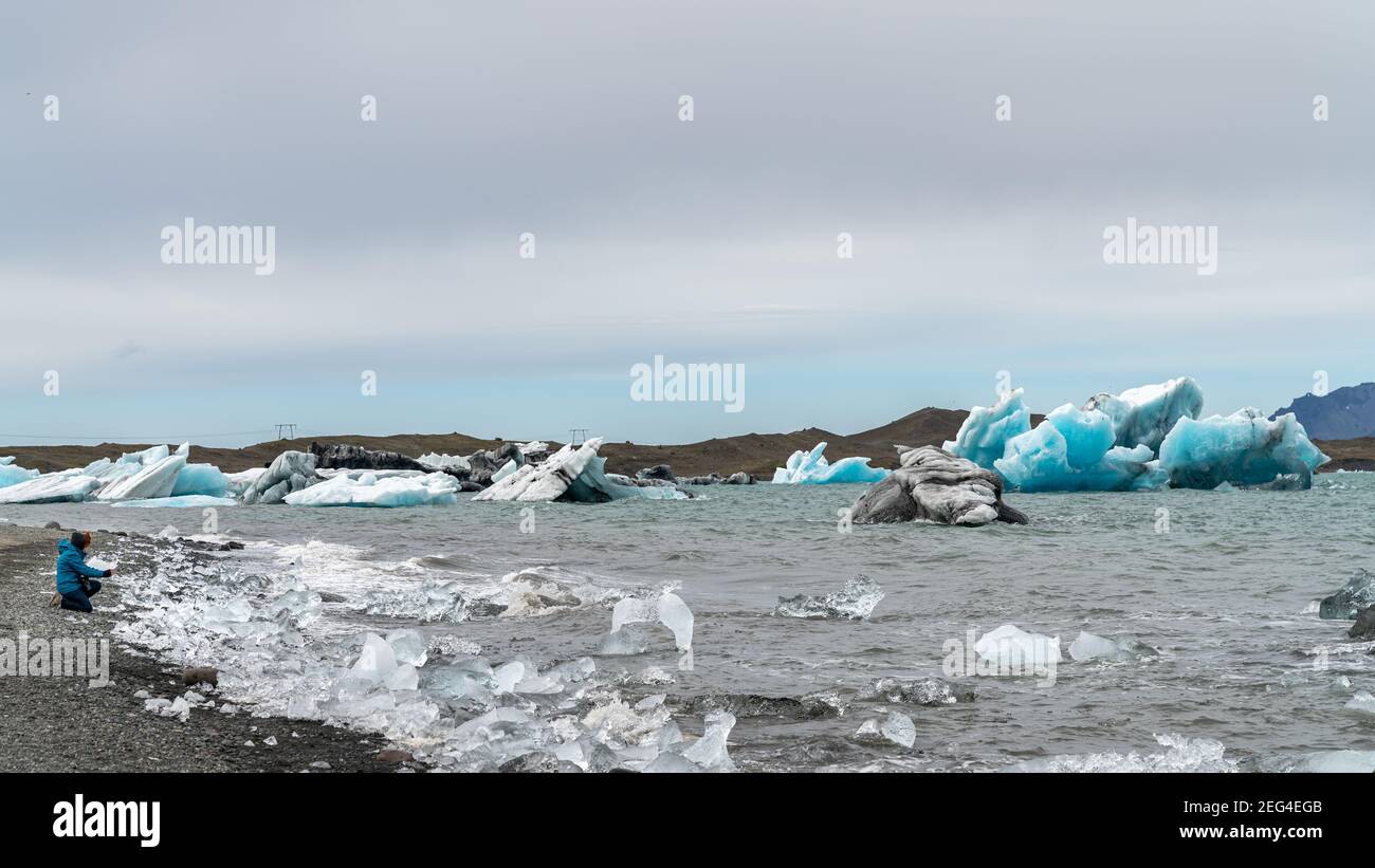 Donna non identificata scattando una foto degli iceberg nella laguna glaciale di Jokulsarlon formata con ghiaccio fondente, Islanda, riscaldamento globale e concep del cambiamento climatico Foto Stock