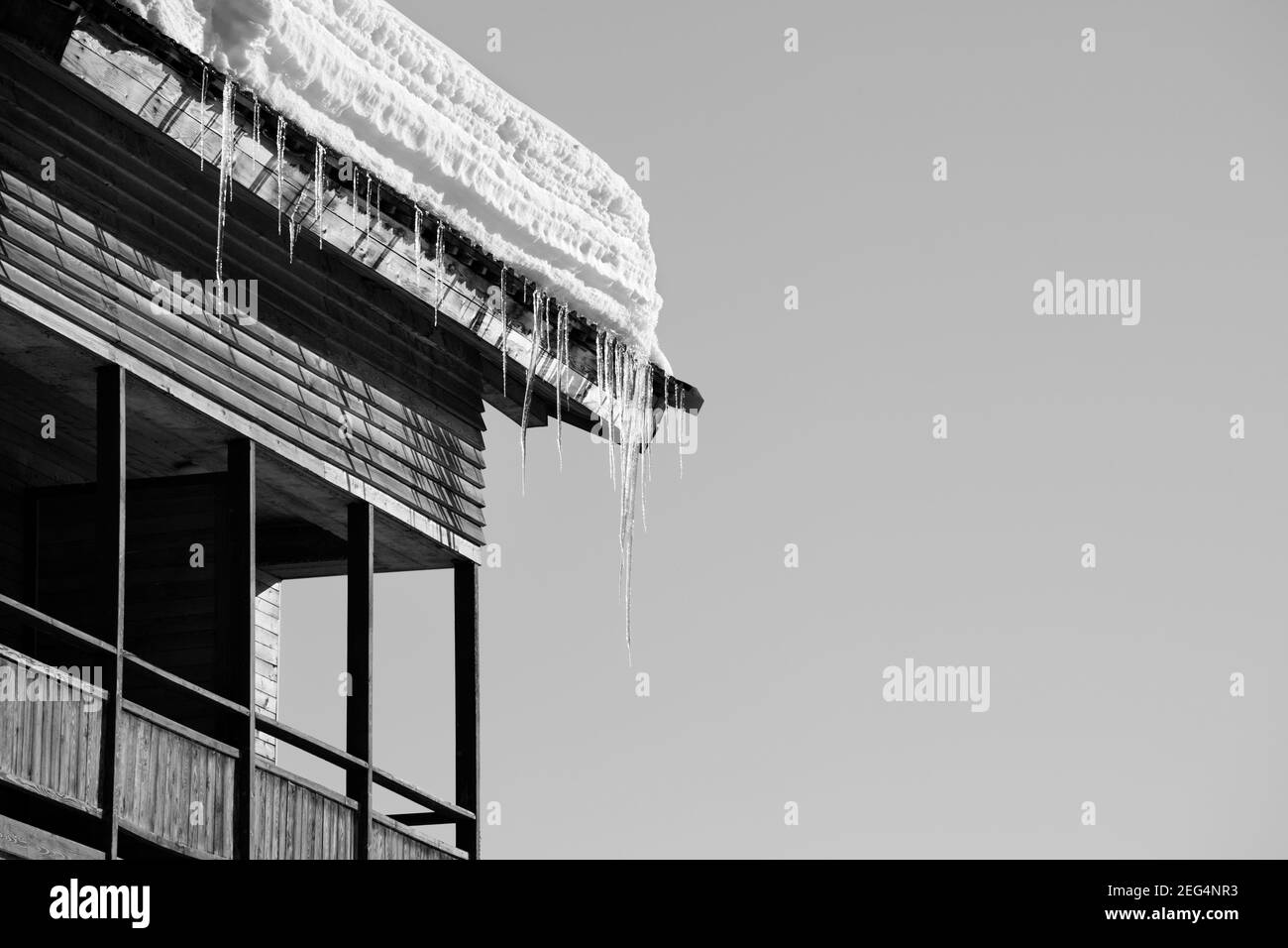 Tetto con neve cornicione e cicale in casa di legno con balcone e cielo chiaro al sole giorno d'inverno. Immagine in bianco e nero. Foto Stock