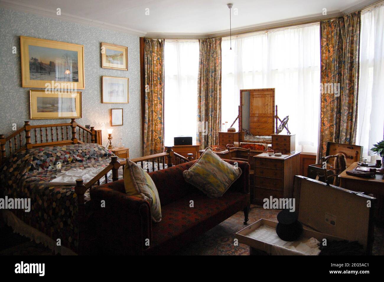 Camera da letto in Cragside Northumberland UK divano vecchia casa grande foto muro arte letto vittoriano cuscini oro cornice ringhiera tende in legno Foto Stock