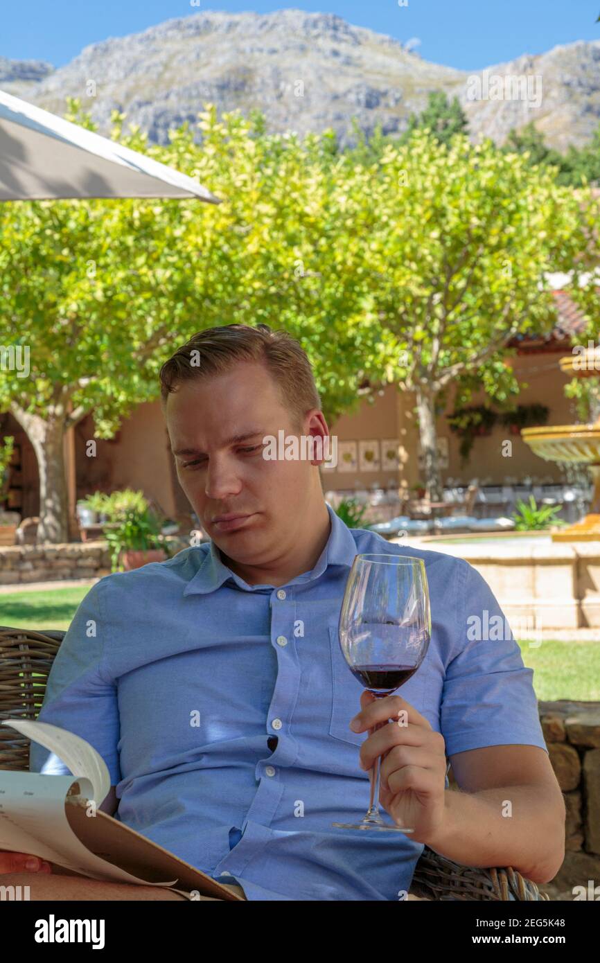 Maschio bianco seduto con un bicchiere di vino in mano che legge il menu, Waterford wine estate, Stellenbosch, Sudafrica Foto Stock