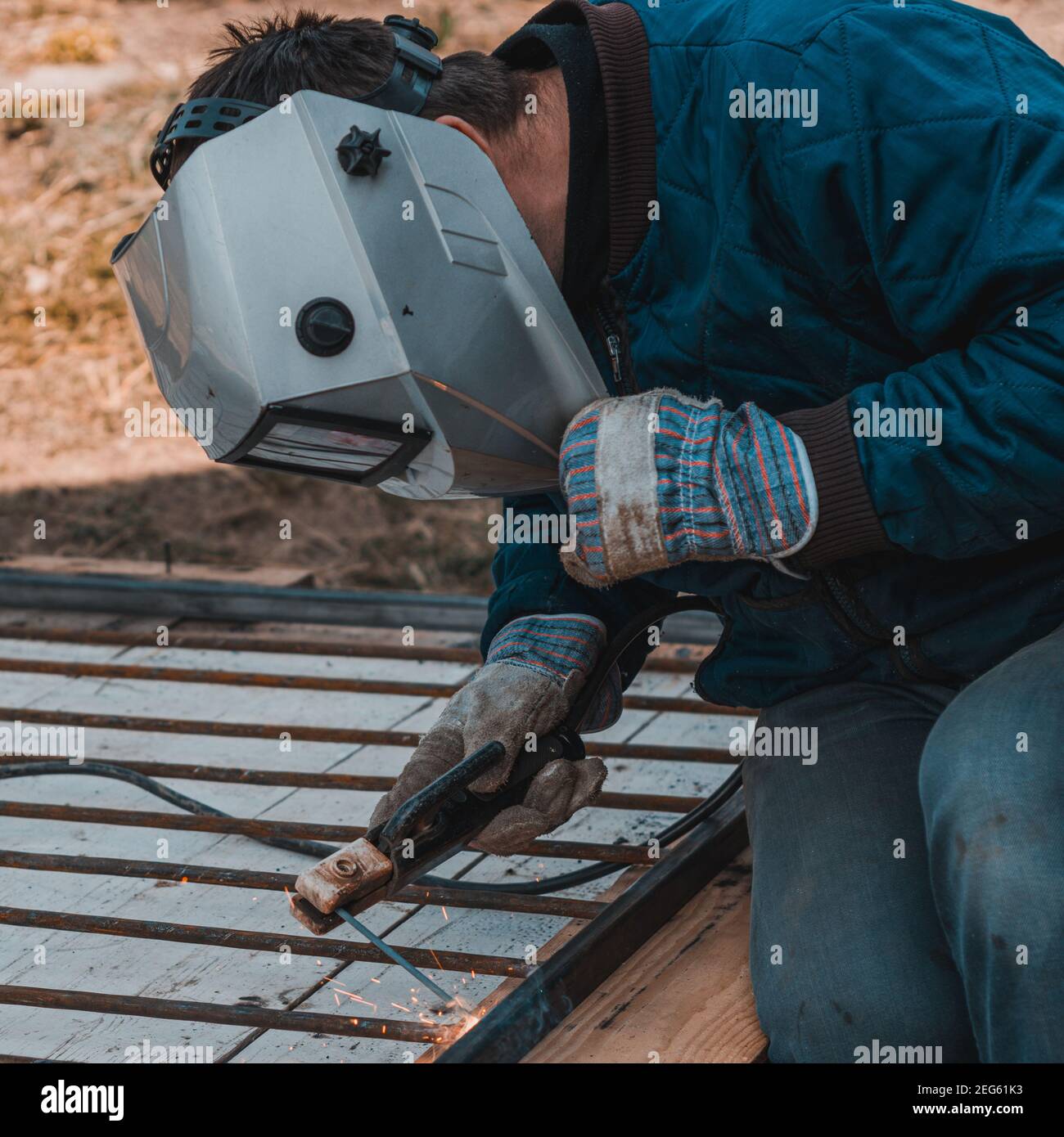 La saldatura del metallo, un lavoratore in una maschera protettiva contro la luce brillante e scintille, un robot sulla strada.2020 Foto Stock