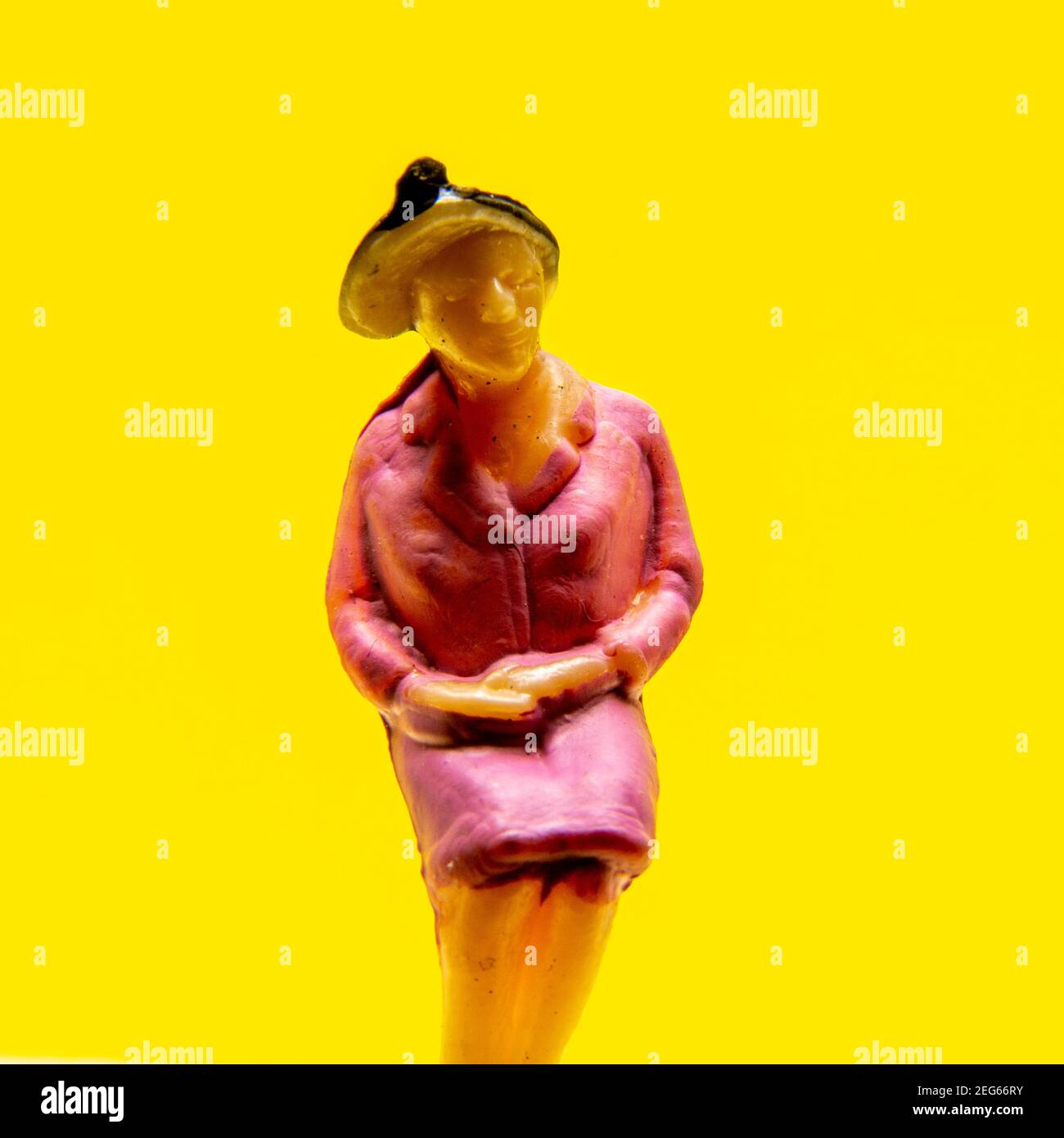 Figura colorata di una donna seduta con un cappello su uno sfondo giallo brillante Foto Stock