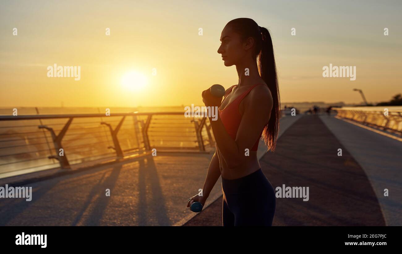 Esercizi mattutini con manubri in condizioni di quarantena. Concetto di stile di vita sano. Allenati con i manubri all'alba. Il sole splende Foto Stock