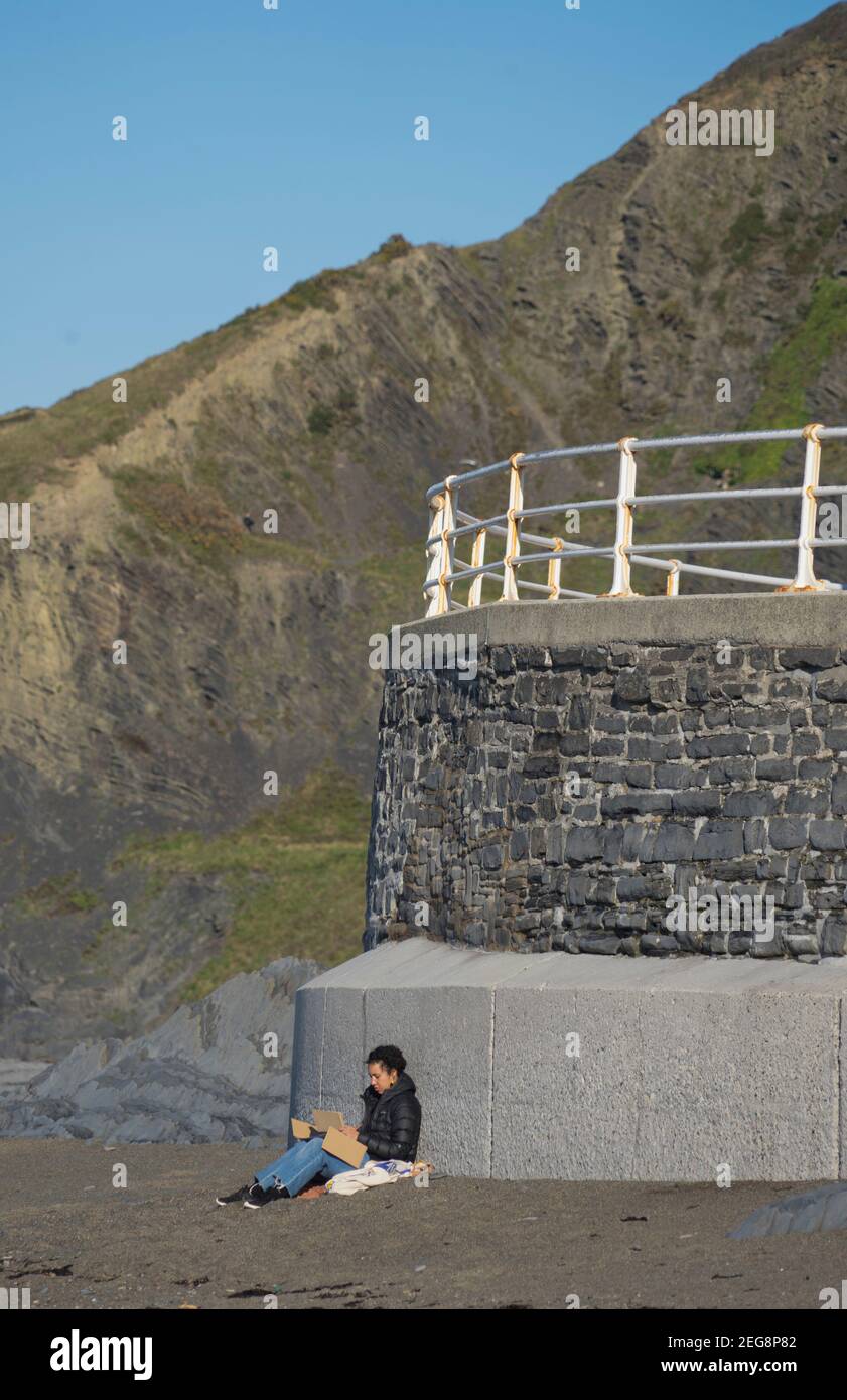 Donna che legge e godendo il sole al lungomare di North Beach, Aberystwyth, Ceredigon, Galles, Regno Unito Foto Stock