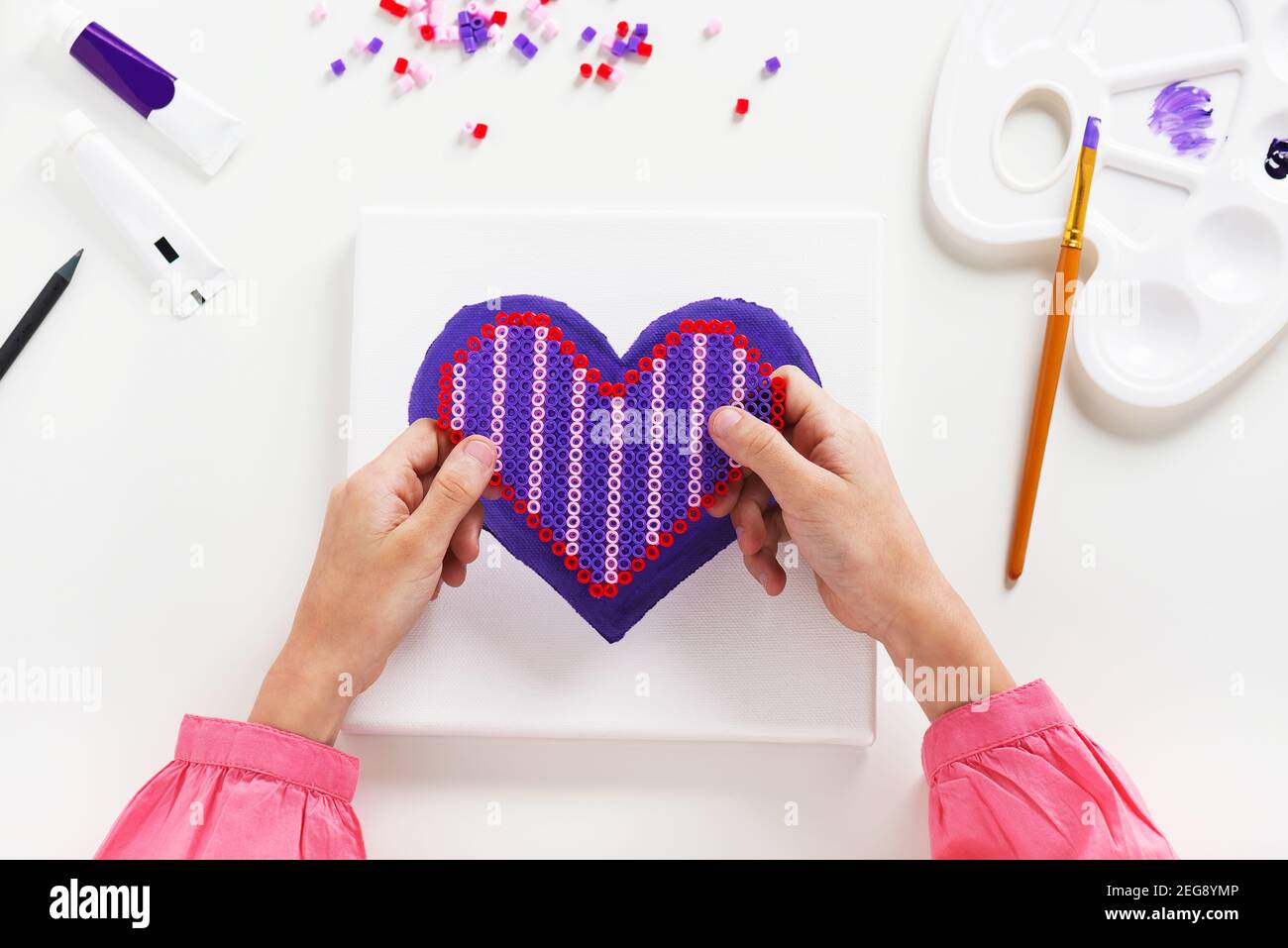Perline arti a forma di cuore e sfondo di vernice acrilica su tela. Artigianato per bambini Foto Stock