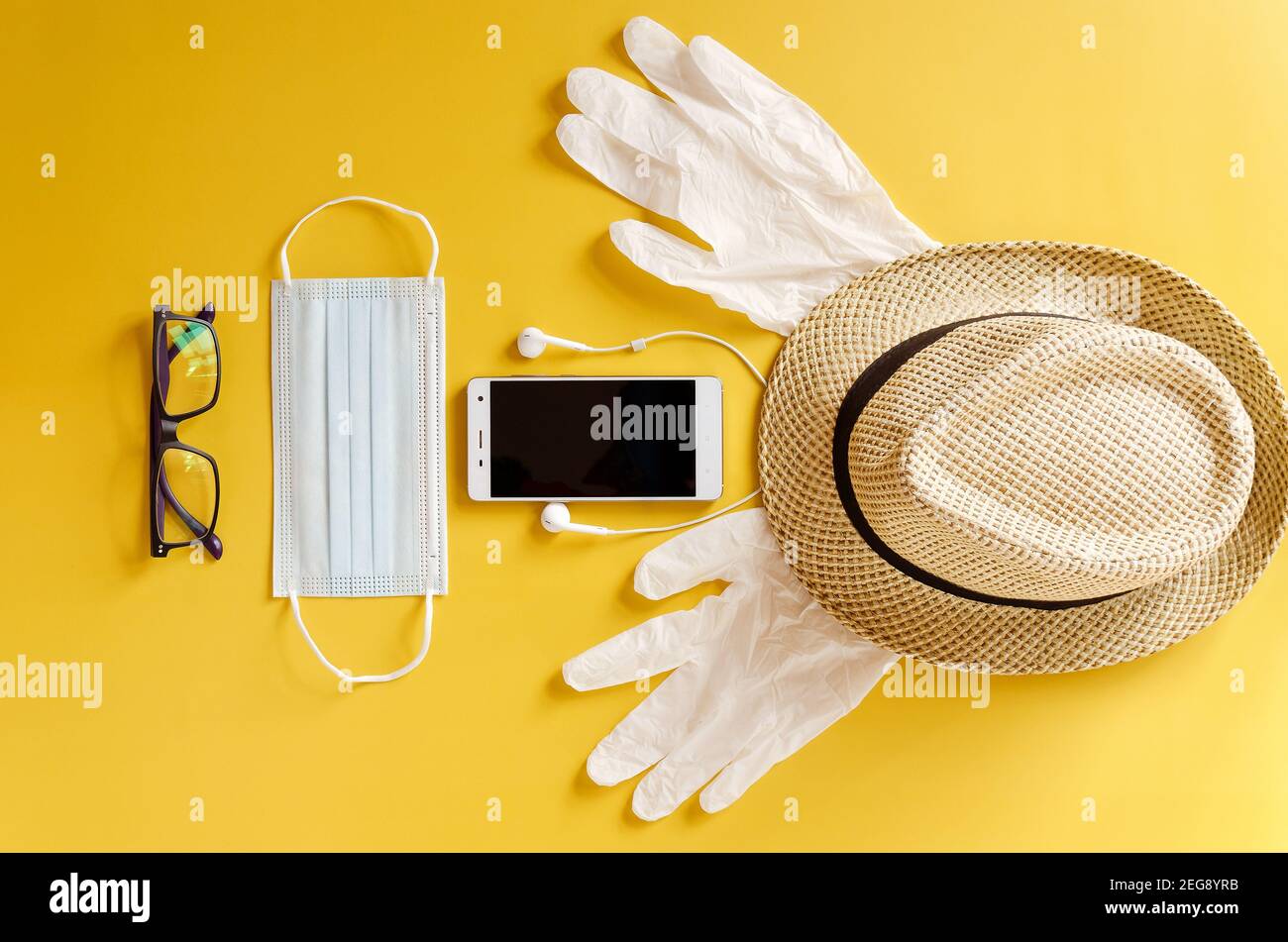 Viaggio dopo Covid-19 e nuovi concetti normali. Vista dall'alto della maschera medica, guanti, cuffie con telefono e cappello da spiaggia su sfondo giallo vicino u Foto Stock