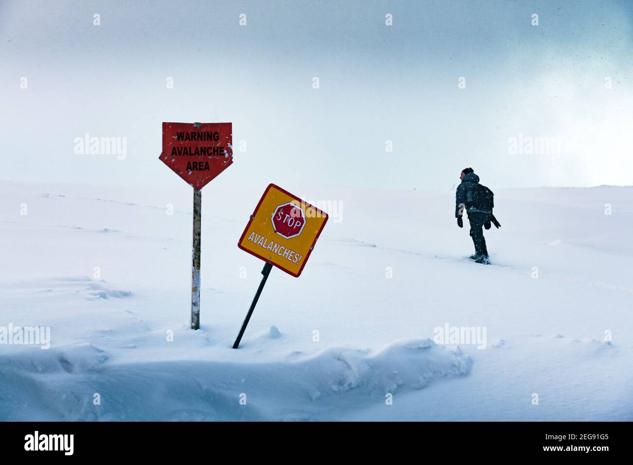 Il turista entra nella zona pericolosa proibita della valanga in inverno. Cartelli di avvertenza sulla neve in primo piano. Concetto di pericolo valanghe Foto Stock
