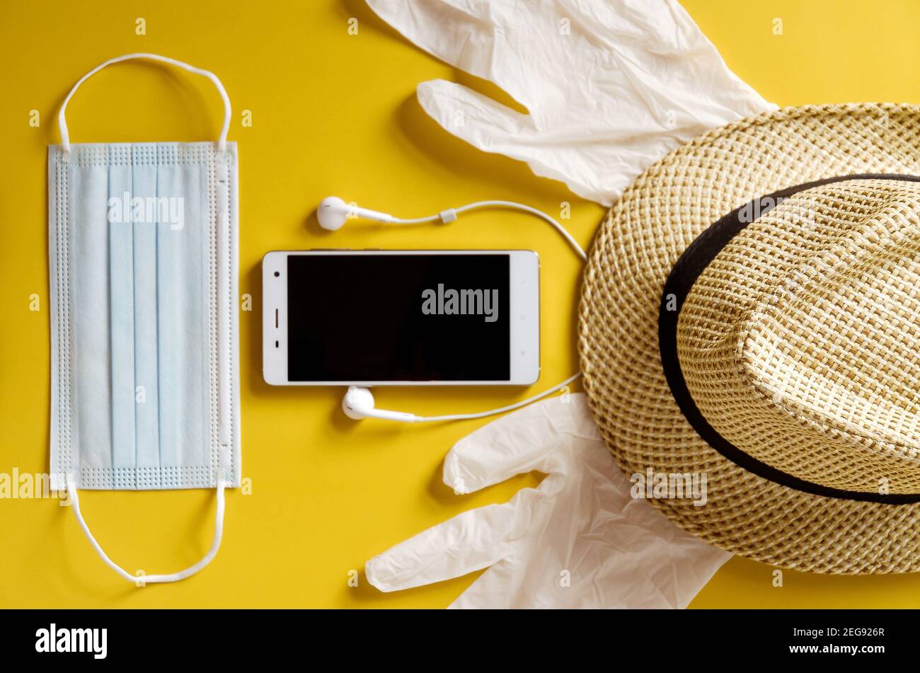 Viaggio dopo Covid-19 e nuovi concetti normali. Vista dall'alto della maschera medica, guanti, cuffie con telefono e cappello da spiaggia su sfondo giallo vicino u Foto Stock