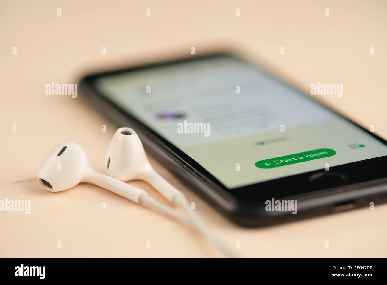 Smartphone sul tavolo di legno con ingresso open Clubhouse nell'app di chat audio e set di cuffie nelle vicinanze. Foto Stock