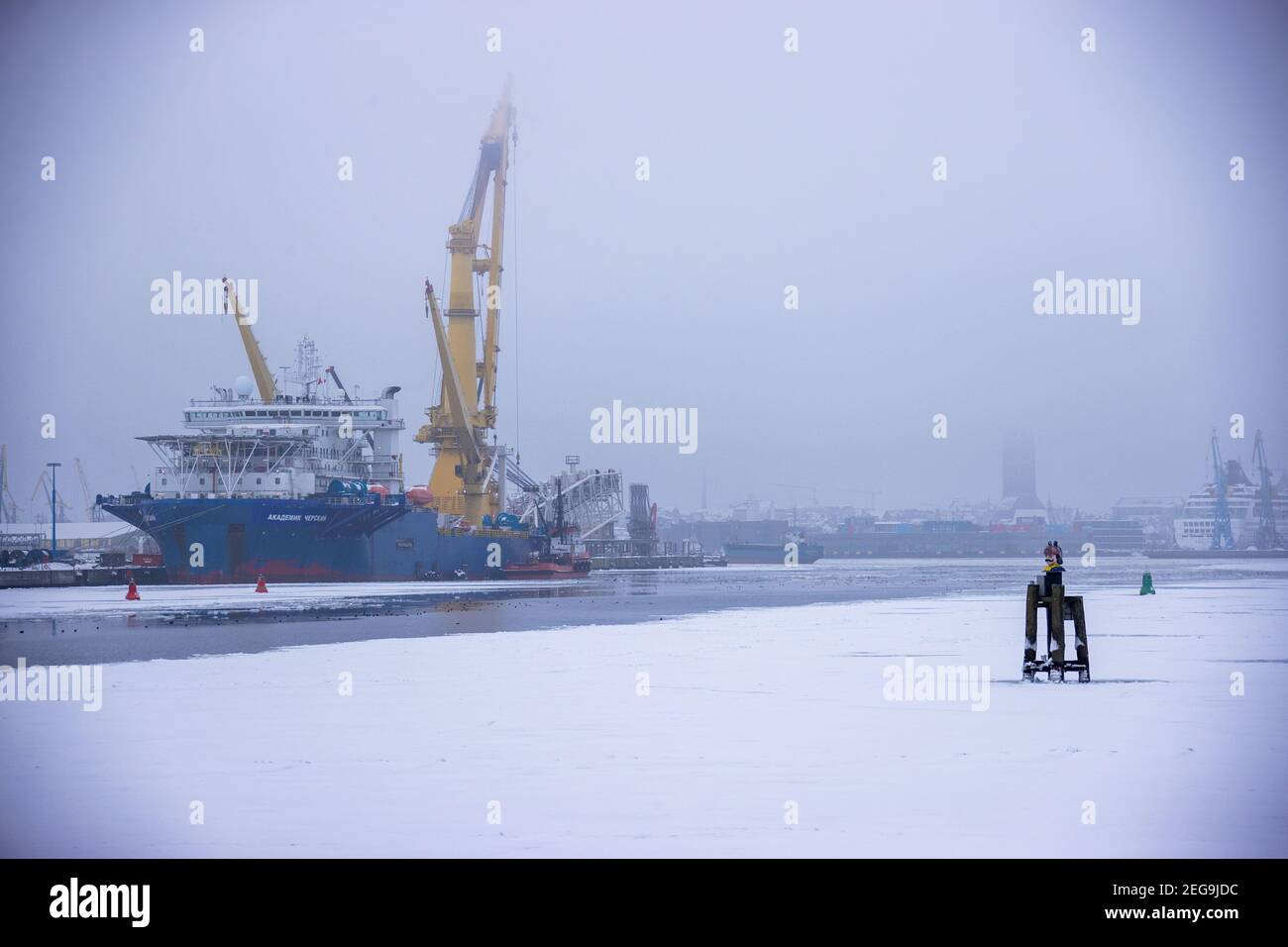 Wismar, Germania. 16 Feb 2021. Un rimorchiatore si trova accanto alla nave russa "Akademik Tscherski", nel porto marittimo parzialmente ghiacciato. La nave speciale è già stata utilizzata per lavori di costruzione del gasdotto tedesco-russo Nord Stream 2 nel Mar Baltico ed è attualmente dotata di ulteriori tecnologie. Sono proseguiti i lavori di posa del gasdotto nei pressi dell'isola di Bornholm. Credit: Jens Büttner/dpa-Zentralbild/ZB/dpa/Alamy Live News Foto Stock