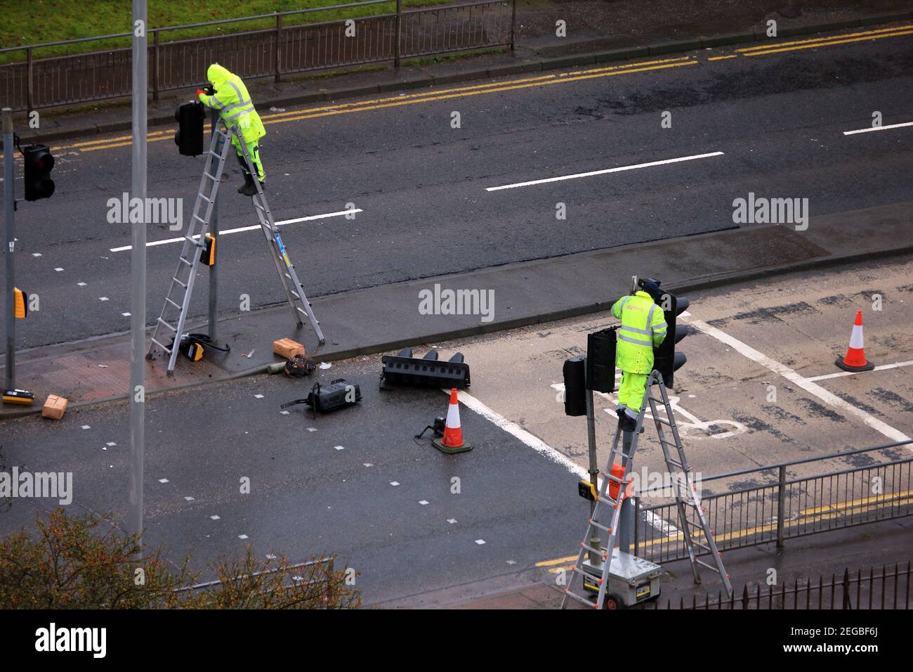 Lavoratori su scale che lavorano su semafori in una giornata bagnata a Paisley, Scozia Foto Stock