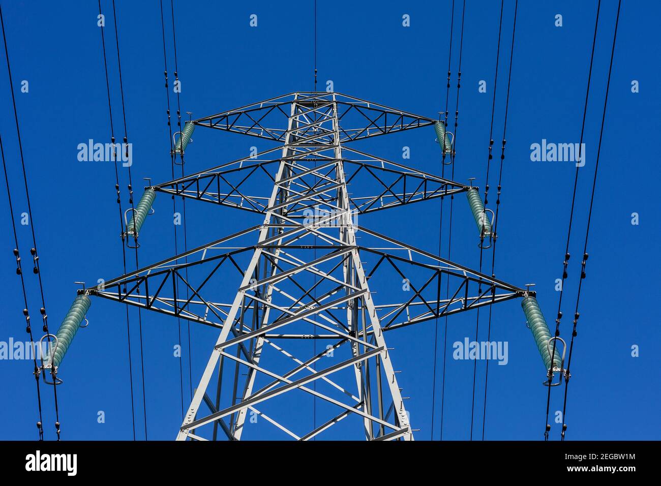 Vista verso l'alto di un traliccio elettrico, cavi di alimentazione e isolatori sospesi contro un cielo blu chiaro Foto Stock