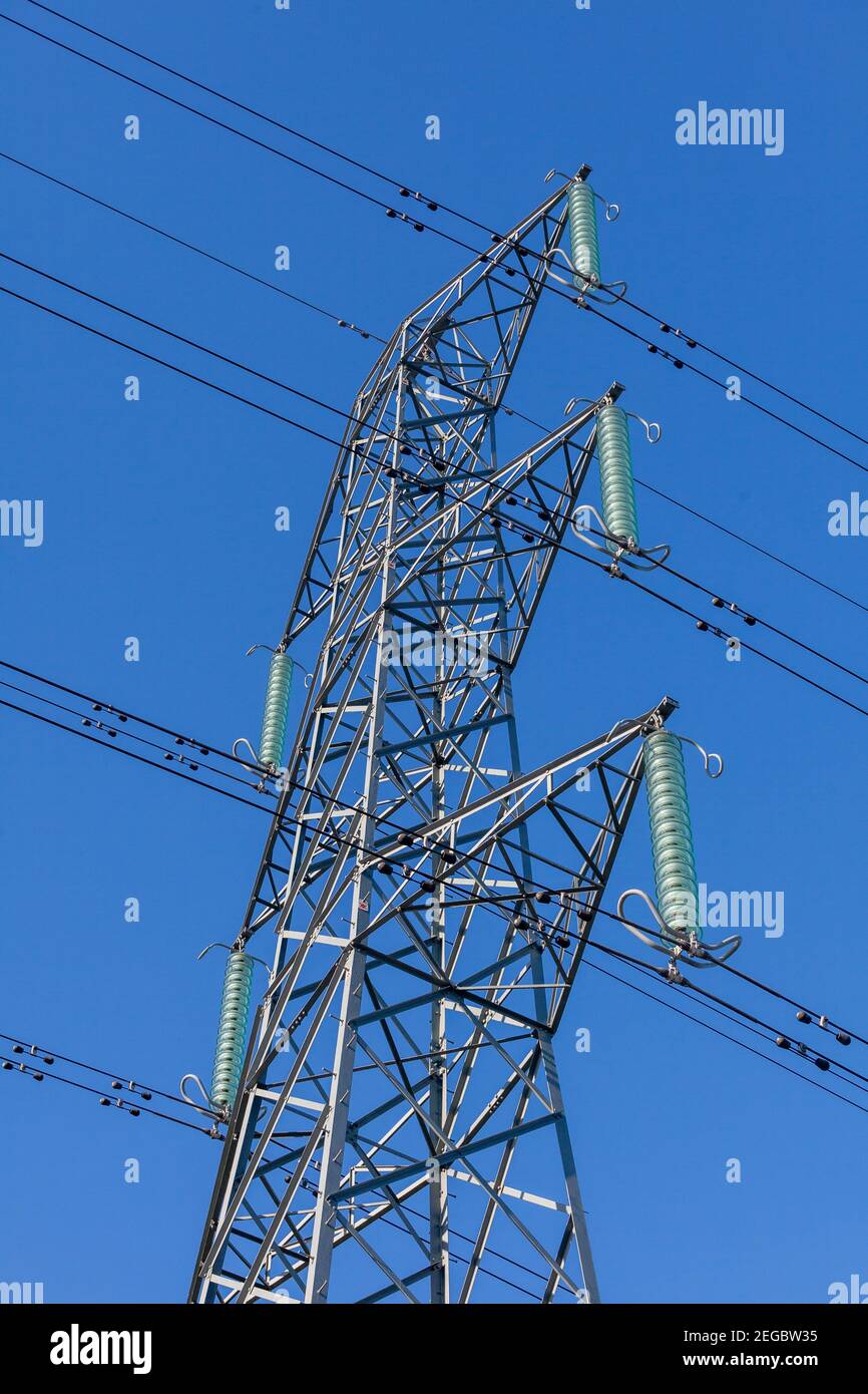 Vista verso l'alto di un traliccio elettrico, cavi di alimentazione e isolatori sospesi contro un cielo blu chiaro Foto Stock
