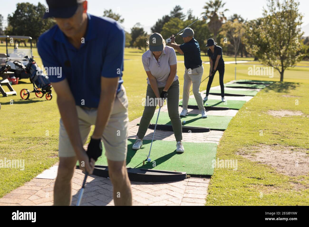 Tre uomini caucasici anziani e una donna che tiene il golf club preparazione per lo scatto sul verde Foto Stock