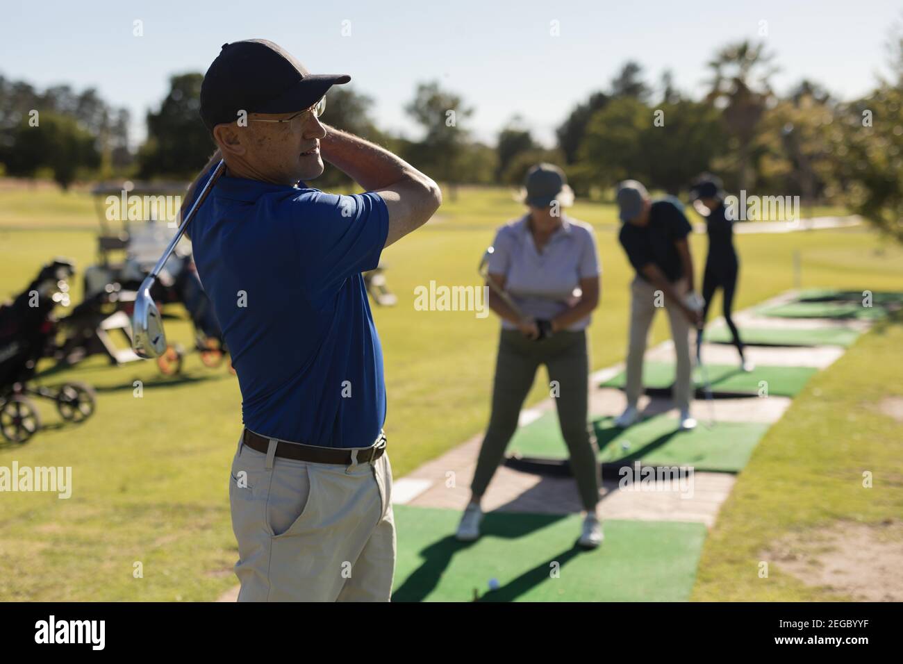 Tre uomini caucasici anziani e una donna che tiene il golf club preparazione per lo scatto sul verde Foto Stock