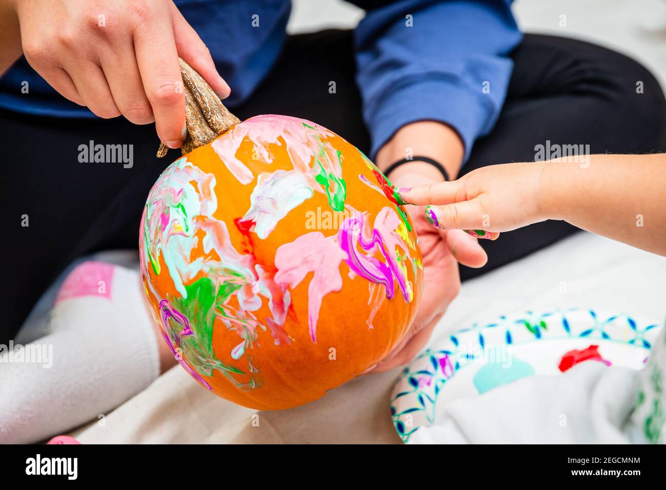 Un dito del bambino irriconoscibile che dipinge una zucca con le vernici colorate mentre un adulto la tiene. Foto Stock