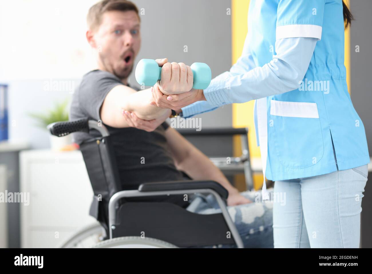 Il medico di riabilitazione aiuta a sollevare il dumbbell al paziente in sedia a rotelle Foto Stock