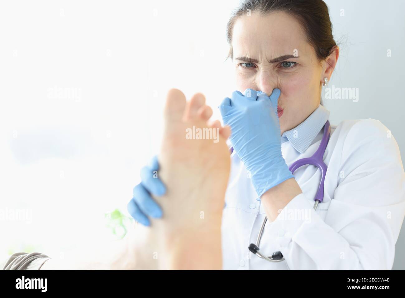 Dermatologo medico che tiene i pazienti piedi e che copre il naso con la mano Foto Stock