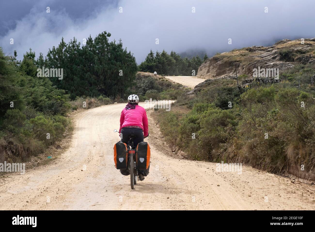 Ciclista femminile in bicicletta pesante carico con grandi panniere su strada sterrata attraverso le Ande, Vallegrande Provincia, Santa Cruz, Bolivia Foto Stock