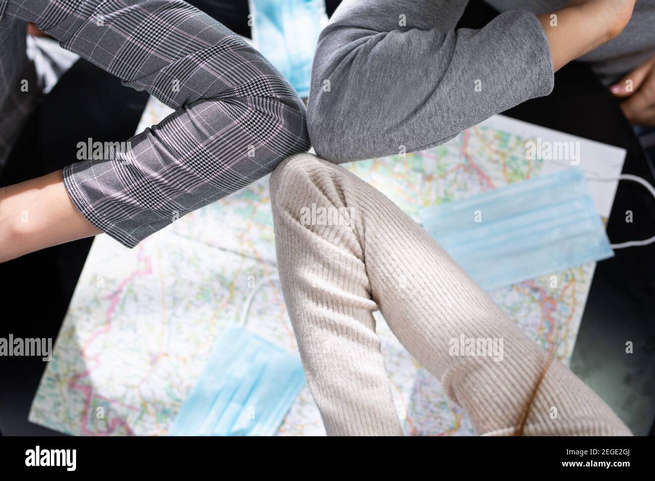 Foto dall'alto sopra il tavolo su cui si trova la mappa del mondo e le maschere mediche. Saluto i colleghi con i gomiti durante la pandemia del covid 19. Foto Stock