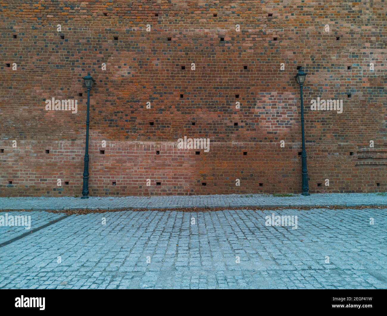 Parete in mattoni rossi con due alte lampade nere vicino al pavimento Foto Stock