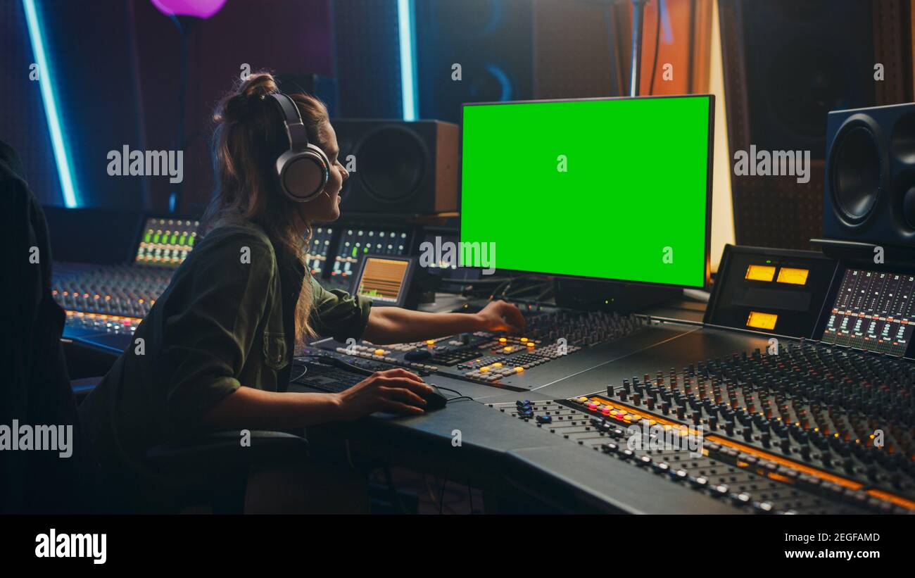 Elegante femmina Audio Engineer Produttore che lavora in Music Record Studio, utilizza cuffie, schermo verde computer Display, Mixer Board, Control Desk a. Foto Stock