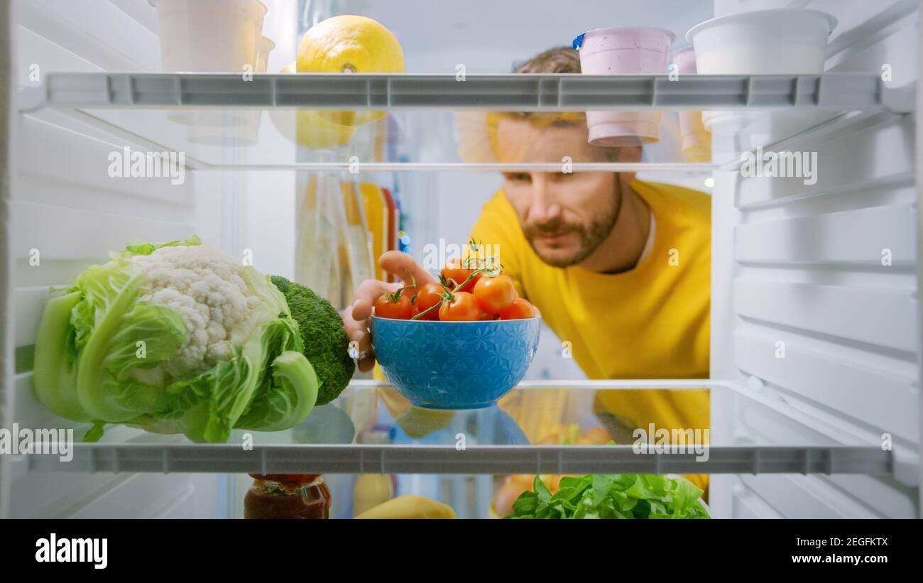 Interno cucina frigorifero: Bell'uomo prende pomodori ciliegia dal frigorifero  aperto. Uomo che prepara un pasto sano. Punto di vista POV Shot da  frigorifero Foto stock - Alamy