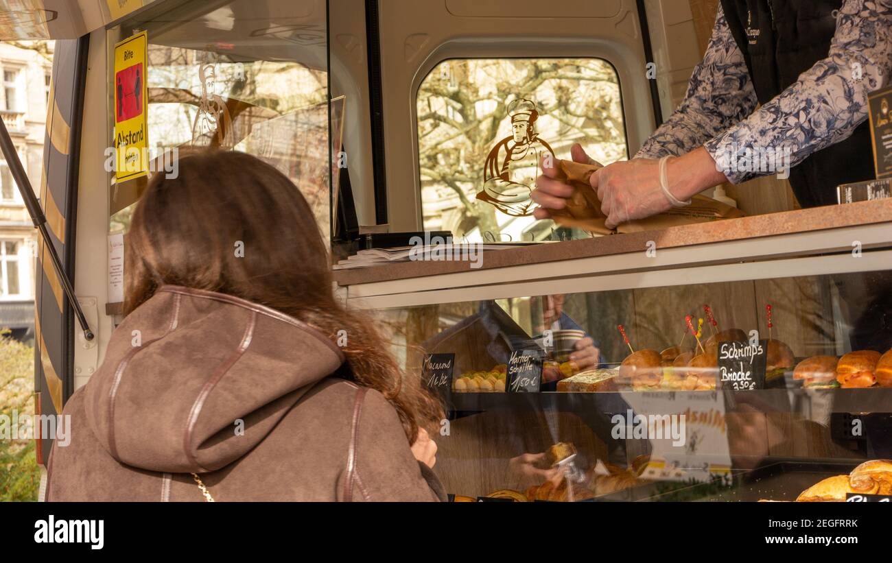 Giovane donna che acquista un pranzo da un chiosco gourmet all'aperto che offre panini, pane, caffè da asporto e cibo da asporto nella pausa pranzo. Misura di sicurezza Foto Stock