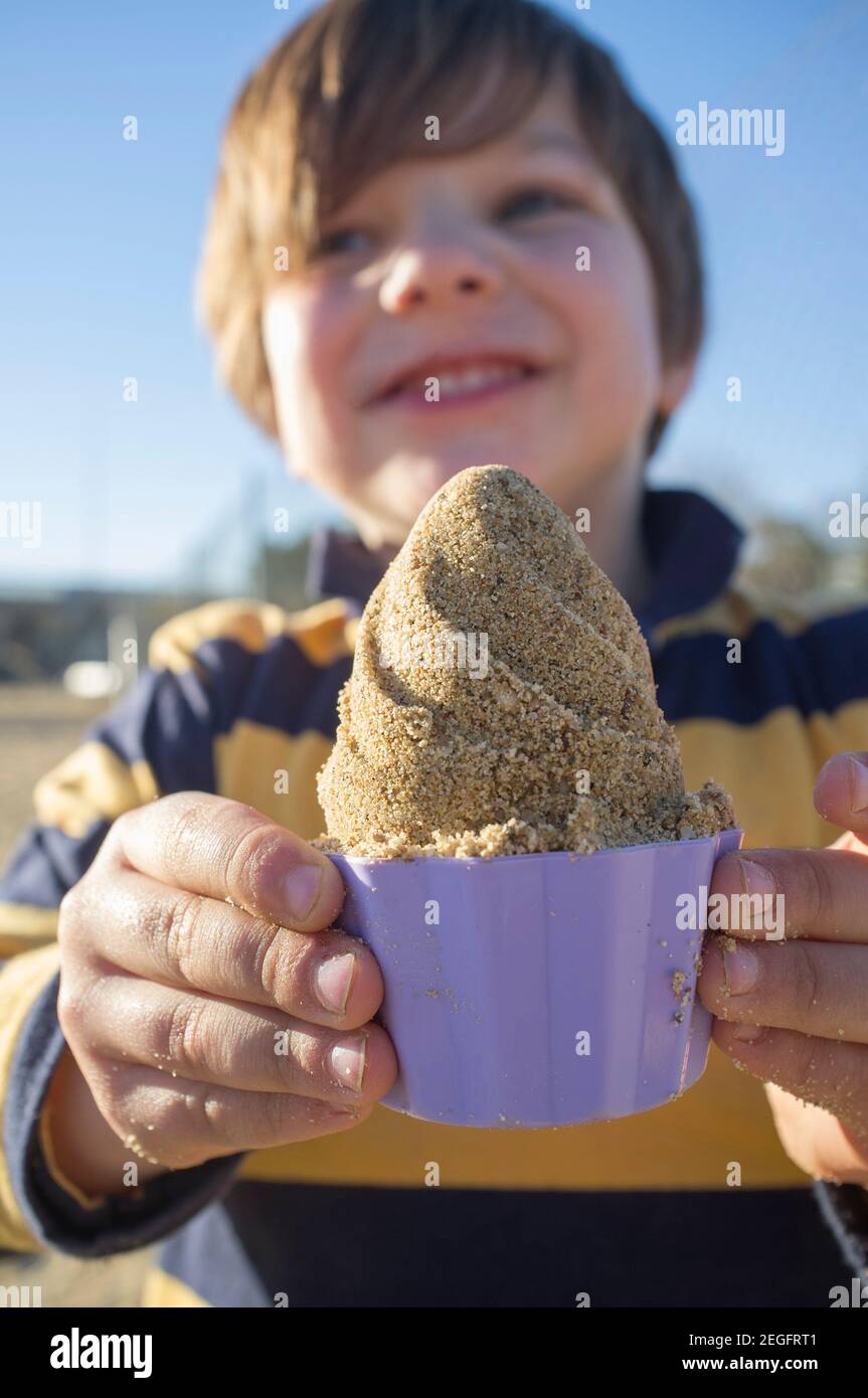 Bambino ragazzo mostra con orgoglio la sua tazza di gelato di sabbia. Luce solare del pomeriggio. Messa a fuoco selettiva Foto Stock