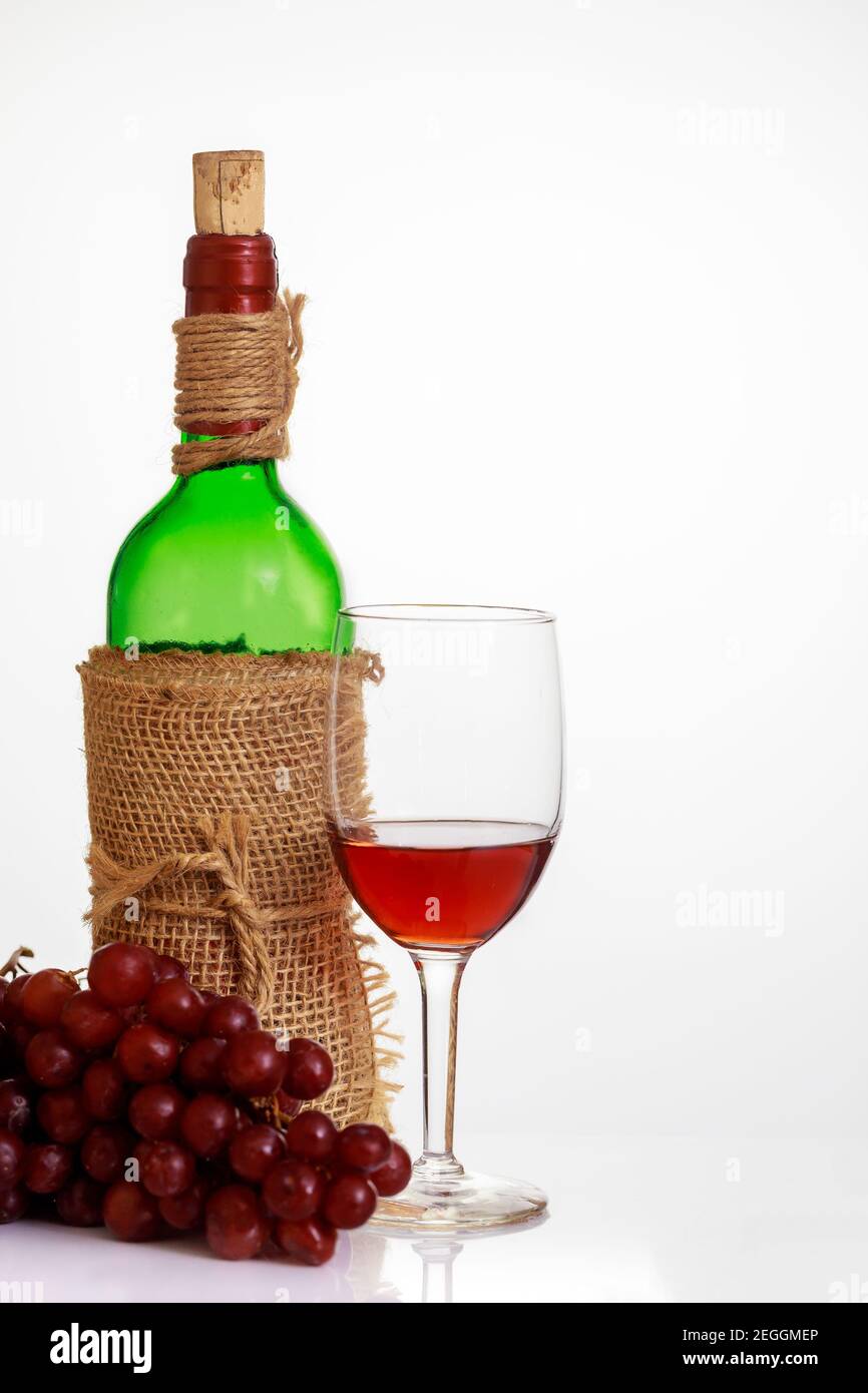 Bicchiere di vino rosso con uva e bottiglia su fondo bianco. Foto Stock
