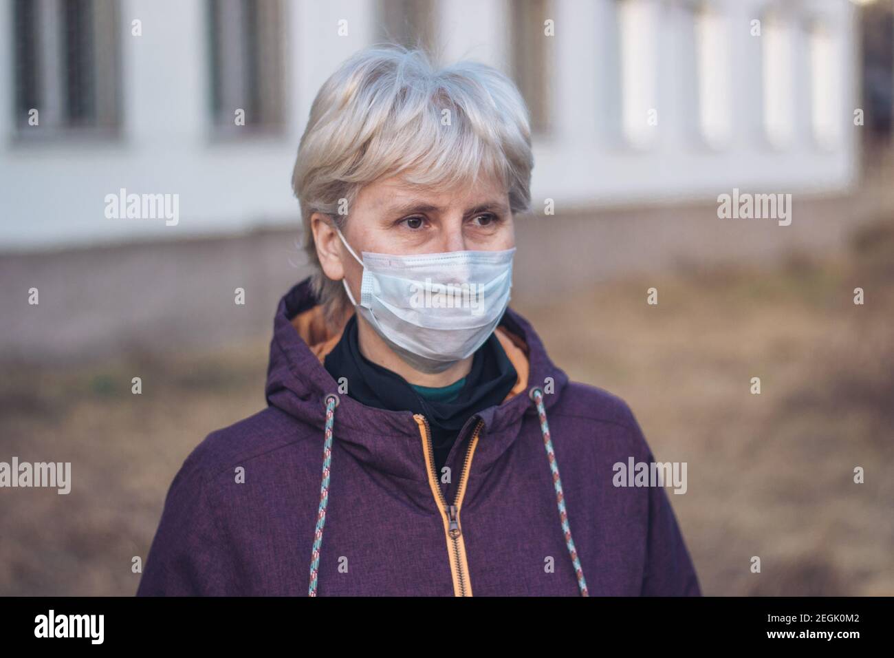 Ritratto di una donna penosa e triste di mezza età in piedi per strada indossando una maschera respiratoria per proteggere la sua salute. Primo piano. Concetto di protezione. Foto Stock