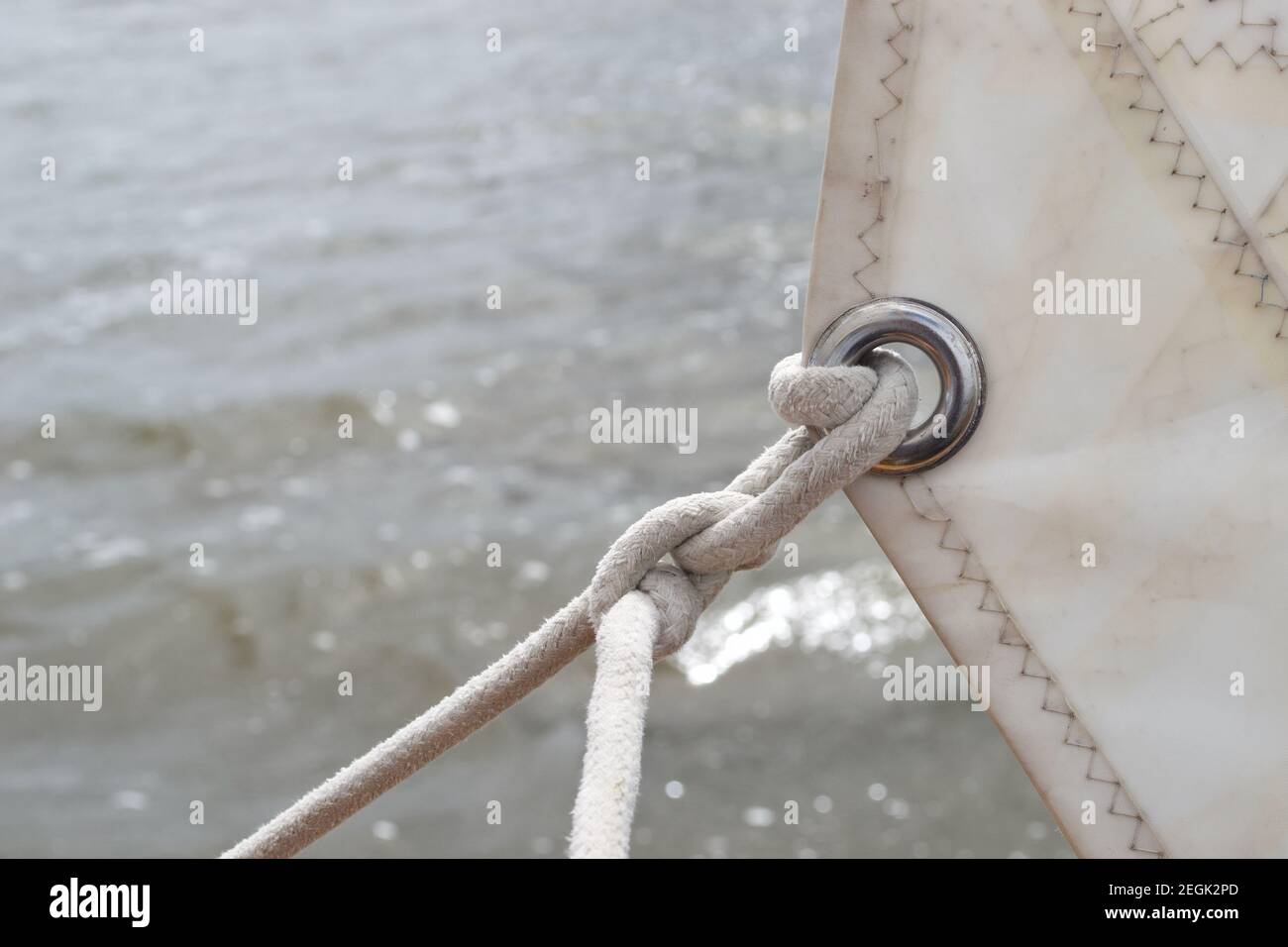 Particolare dell'anello di metallo d'argento (occhiello) in una vela bianca, con una corda annodata bianca attaccata ad esso e tirando stretto (foglio - foglio del braccio) come la vela i Foto Stock