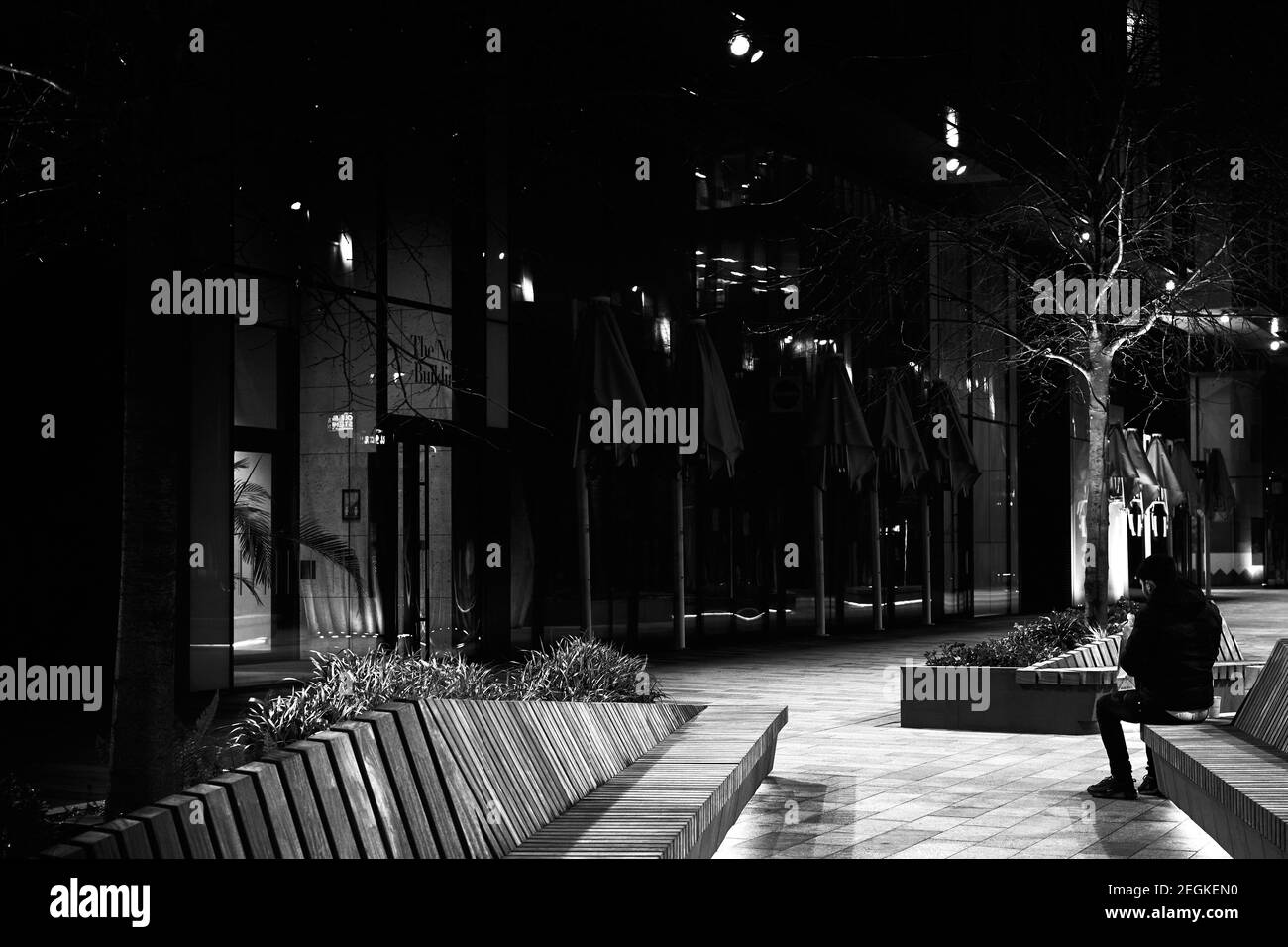 LondonUK - 17 Feb 2021: Immagine monocromatica in bianco e nero dell'uomo mentre mangiava seduto in panchina in una moderna strada urbana contemporanea di notte Foto Stock