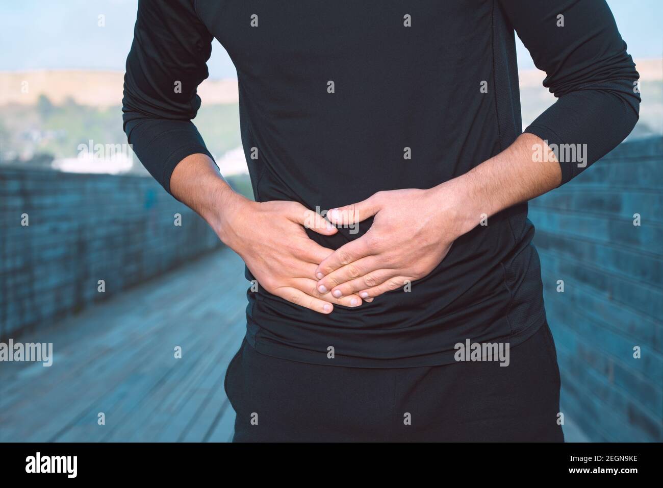 Uomo in abiti sportivi neri che soffrono di cuciture laterali o crampi allo stomaco durante la corsa. Dolore laterale dopo il jogging. Foto Stock