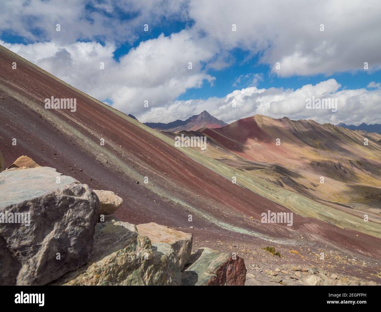 Vinacunca aka Rainbow vista laterale montagna, rocce in primo piano sotto il cielo blu con grandi nuvole bianche Foto Stock