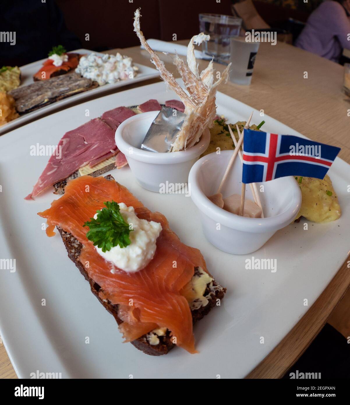 Piatto campione di cibo islandese con squalo fermentato, pesce secco, burro, trota affumicata e agnello, con bandiera islandese in cima Foto Stock