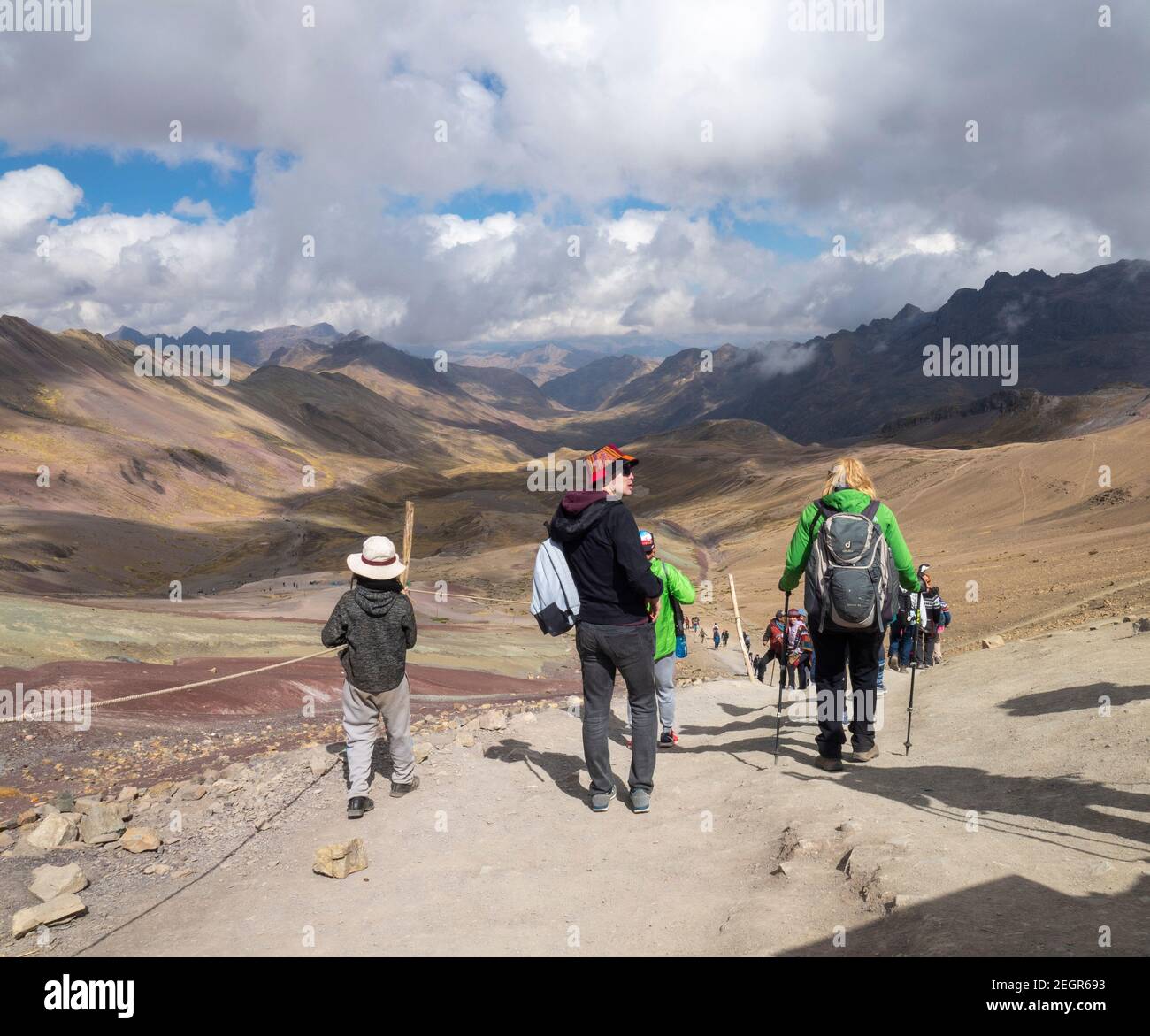 Perù, Vinicunca - 1 ottobre 2019 - turisti multipli a piedi giù dalla montagna su sentiero sterrato, molti toni di terra sulla terra e nuvole gettano ombre Foto Stock