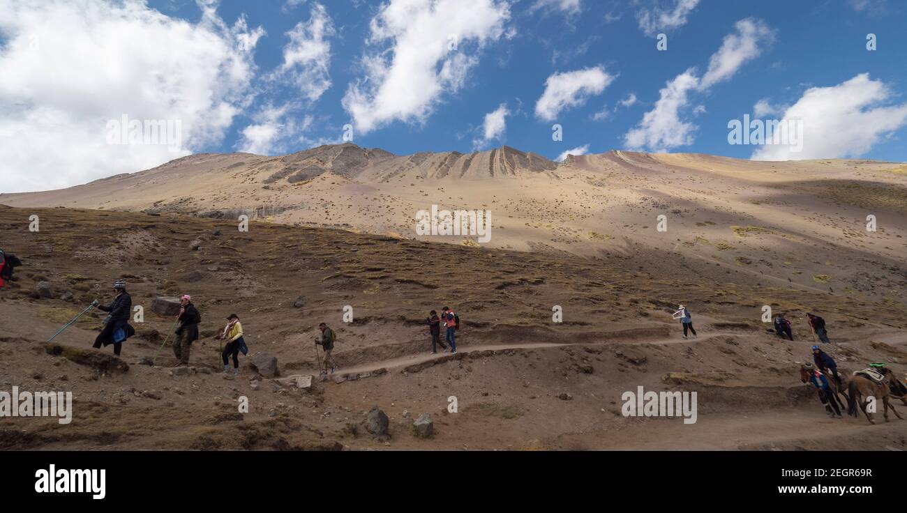 Perù, Vinicunca - 1 ottobre 2019 - i turisti camminano lungo il sentiero sterrato accanto alla catena montuosa sotto il cielo blu Foto Stock