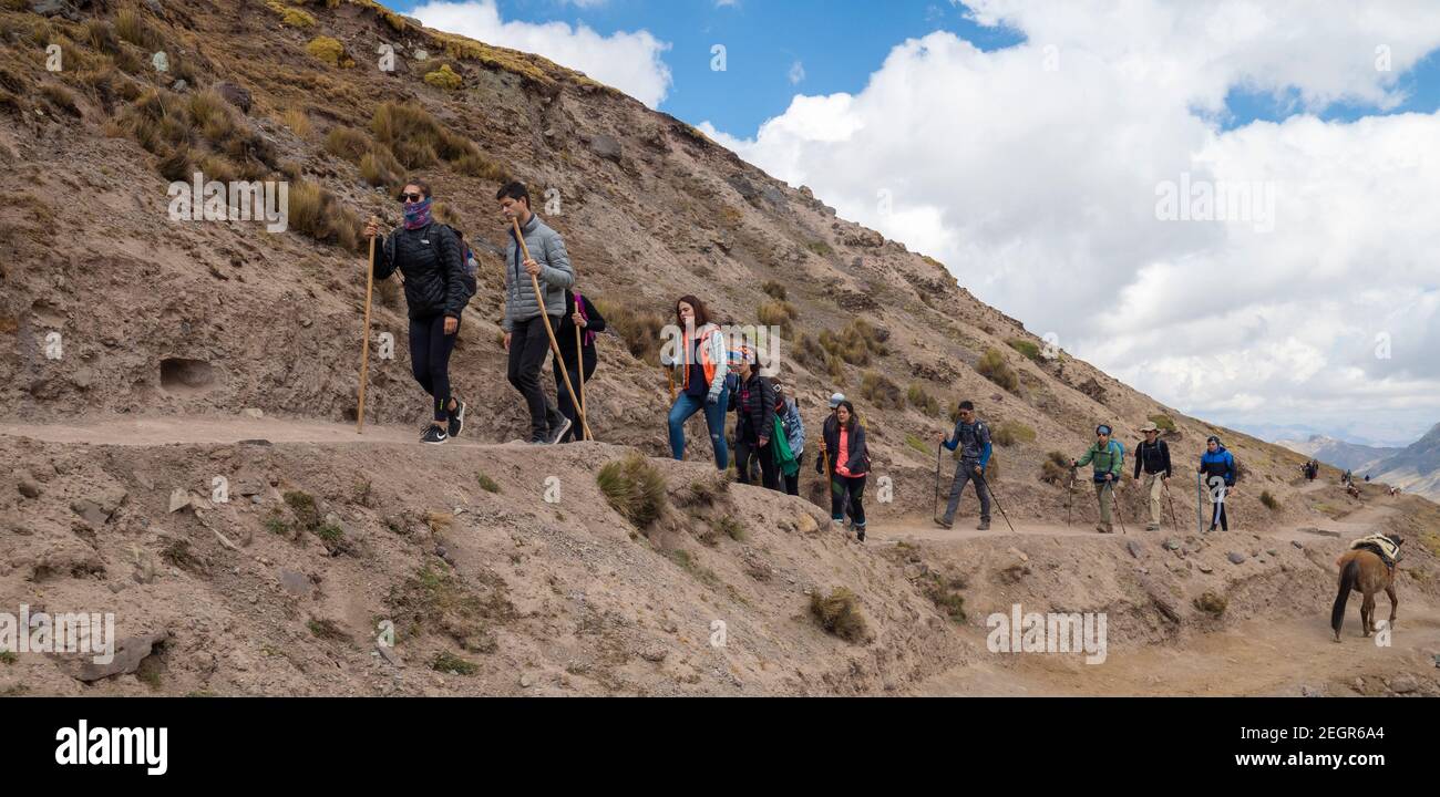 Perù, Vinicunca - 1 ottobre 2019 - escursionisti a piedi giù sentiero sterrato accanto alla montagna sotto il cielo blu Foto Stock