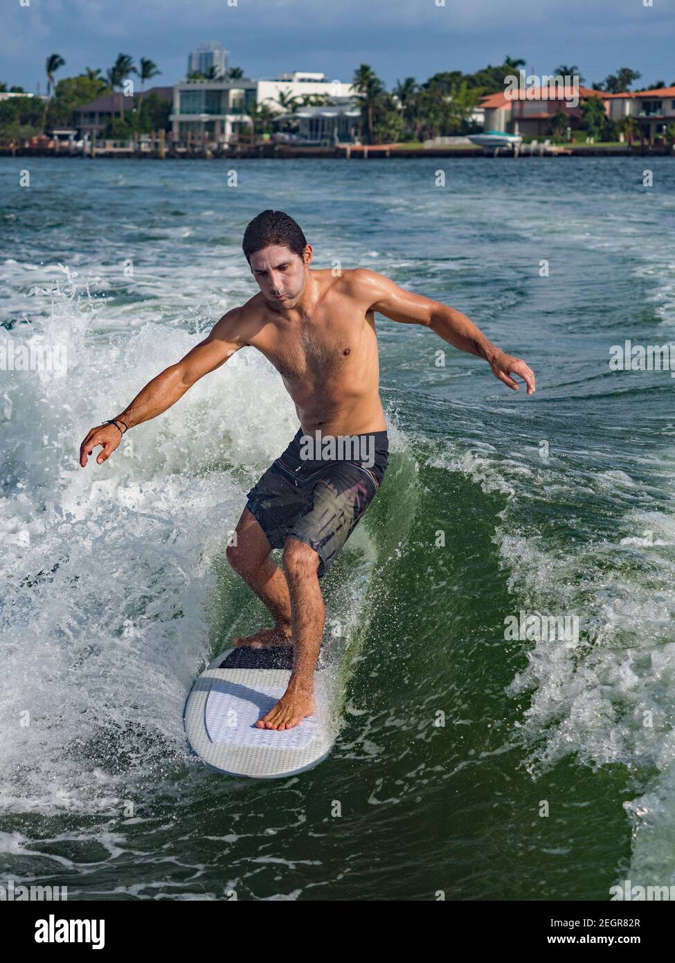 L'uomo atletico cavalca un'onda mentre si wakesurf a Miami, indossando la protezione solare sul viso Foto Stock