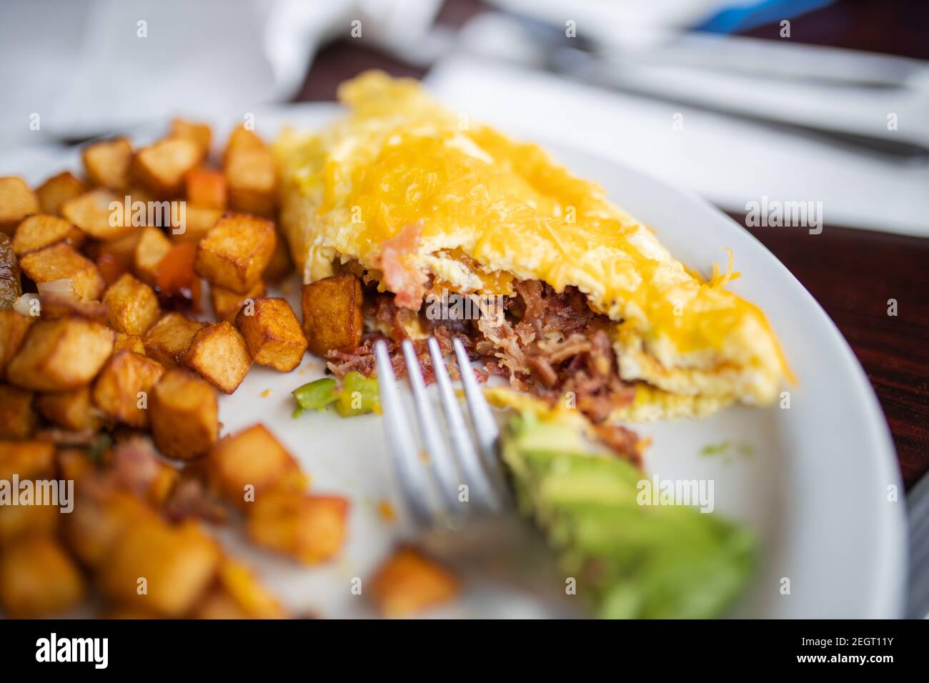 Omelette e patate arrostite mangiate a metà su un piatto bianco Foto Stock