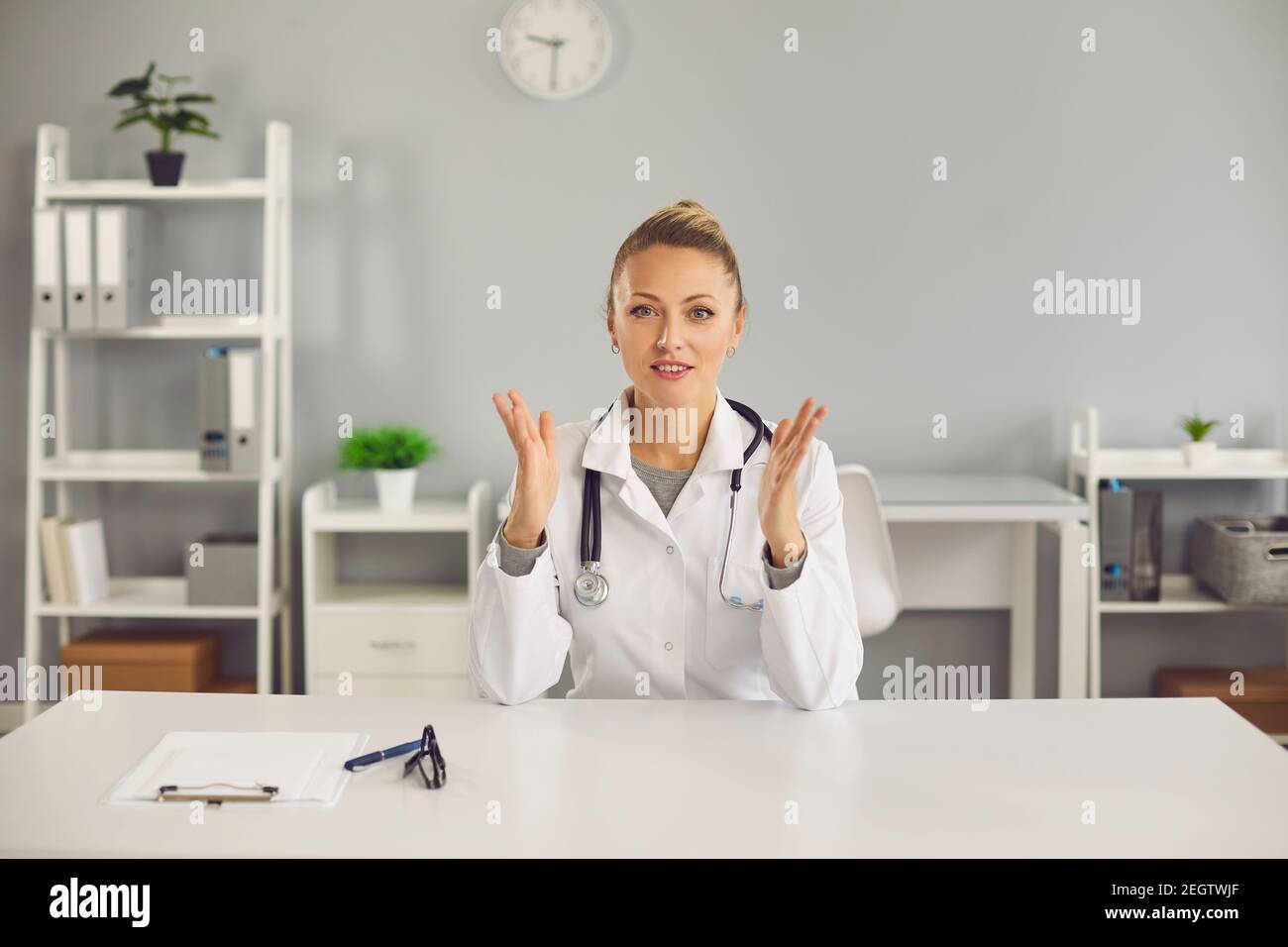 Giovane positivo biondo femmina medico infermiera terapeuta seduta, parlando online con paziente Foto Stock